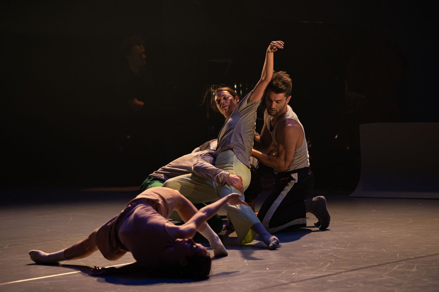 Modern dancers perform an expressive lift sequence on a dark stage during a contemporary dance performance.