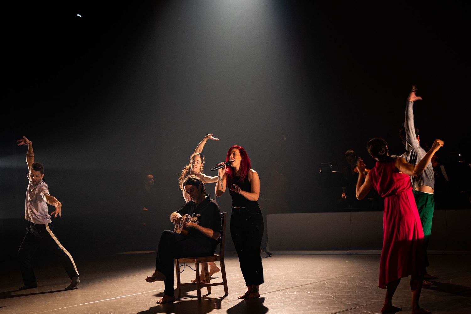 Dancers performing on dimly lit stage with dramatic spotlight overhead during emotional contemporary dance piece.