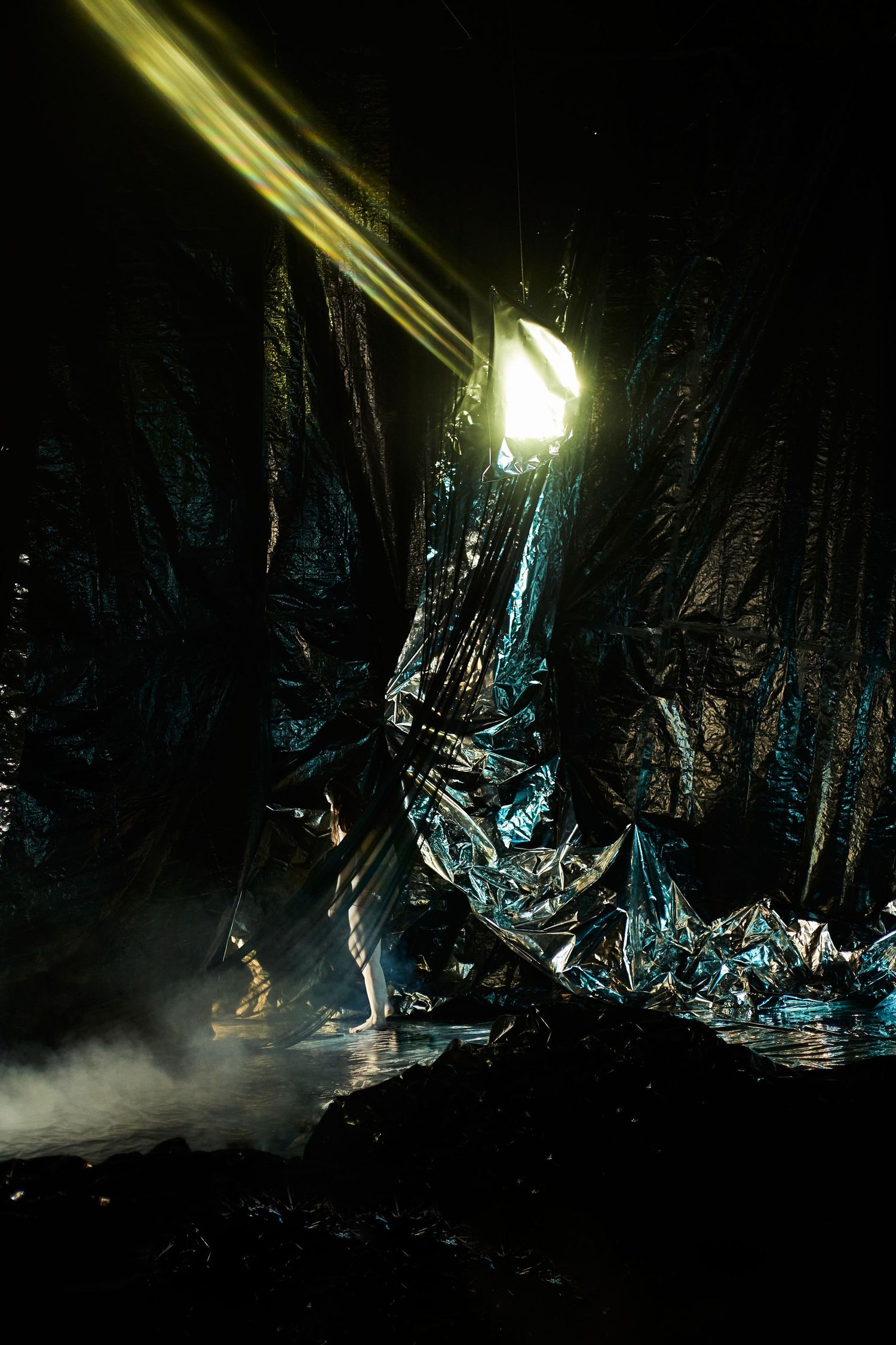 A bright beam of light illuminates jagged crystalline formations in a dark cave with misty atmosphere.