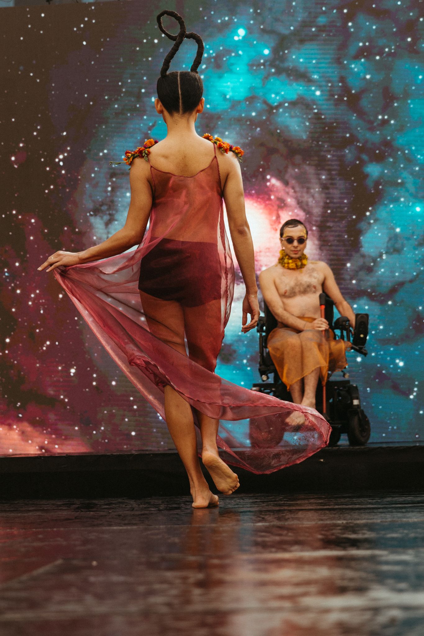 Dancers perform in flowing red costumes against a starry blue digital backdrop on stage.