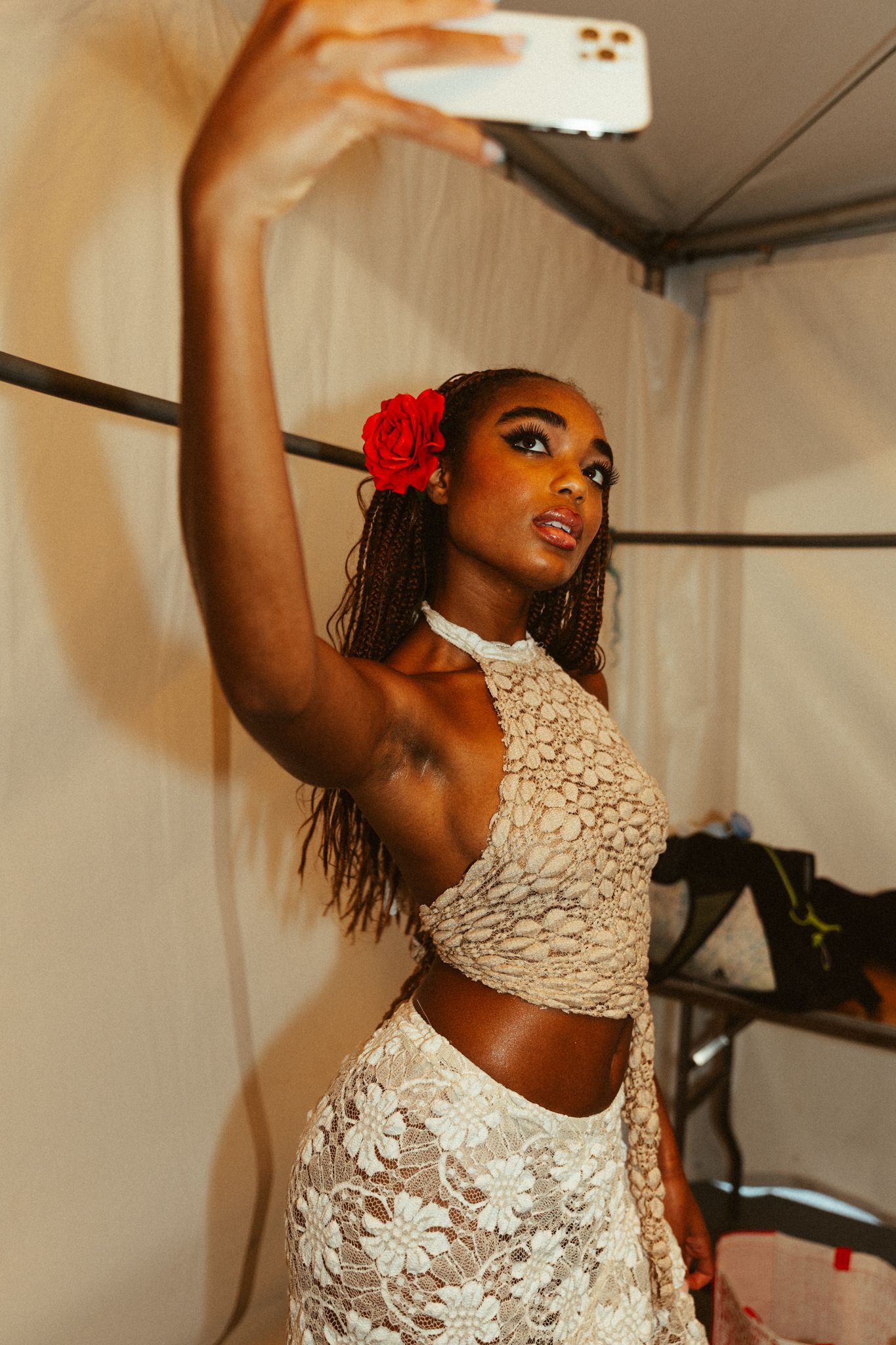 A dancer in a white lace two-piece outfit and red flower accessory poses elegantly while taking a selfie.