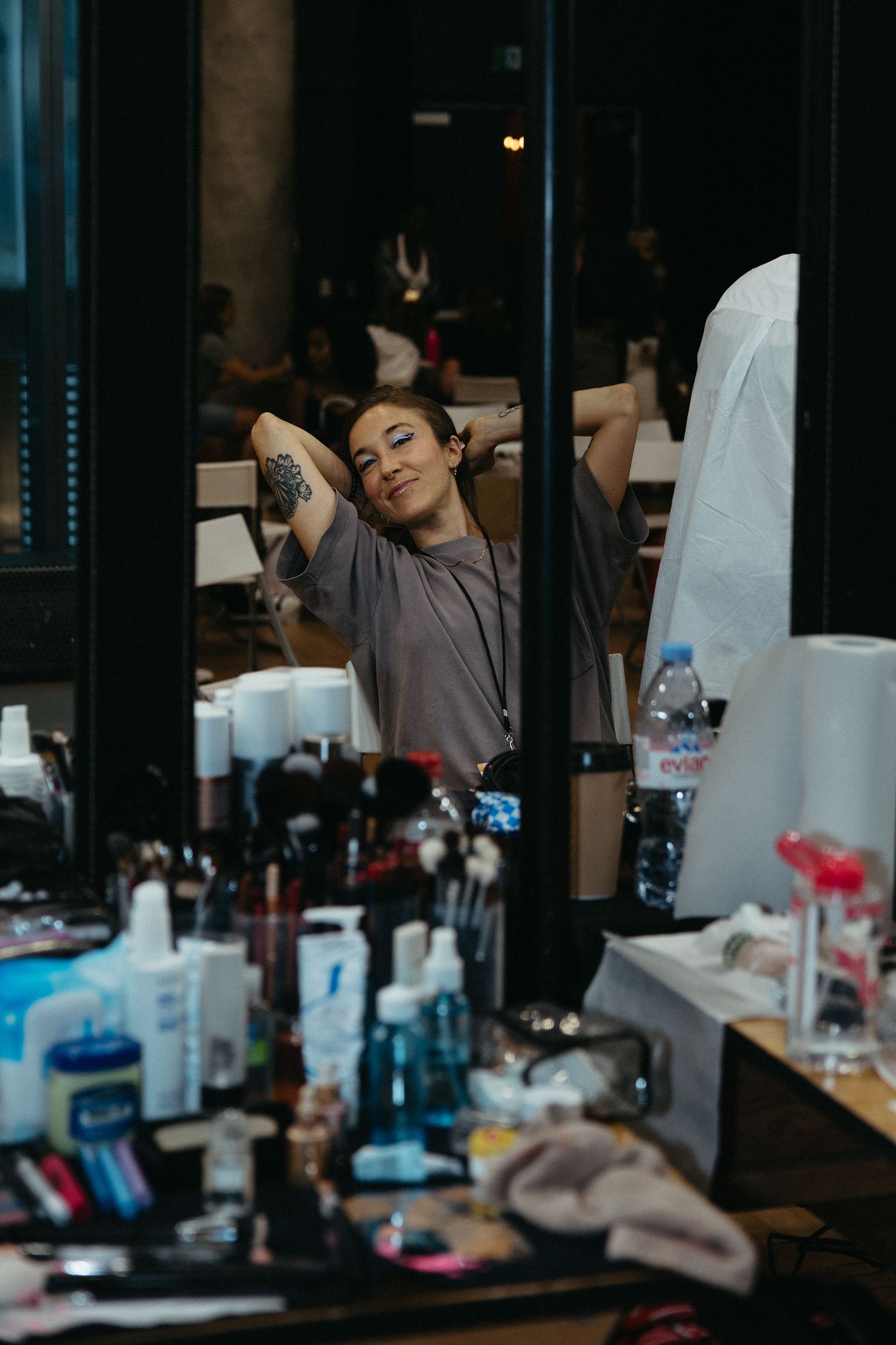 Someone stretches in a chair at a beauty salon surrounded by cosmetic products and styling tools on the counter.
