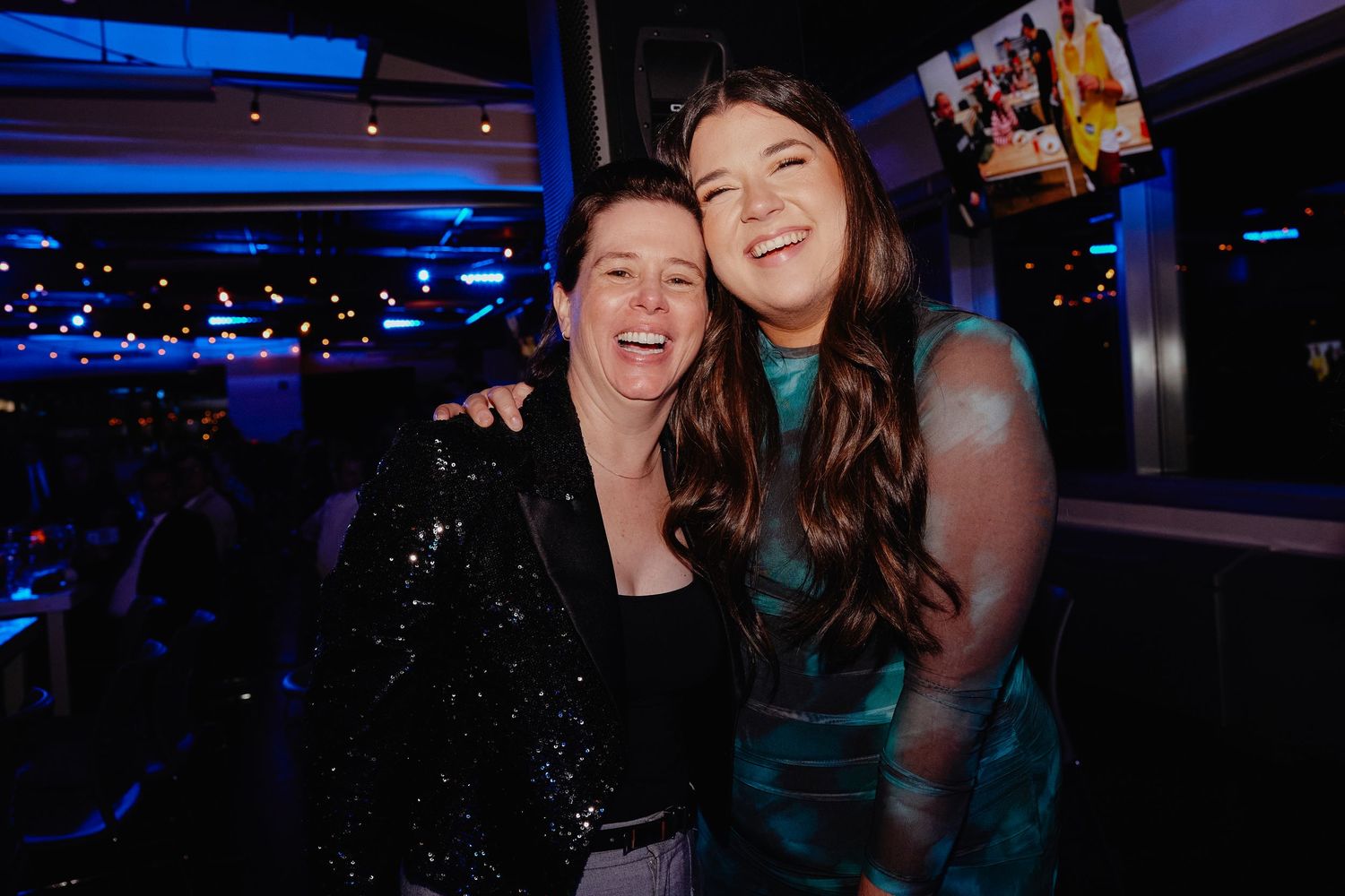 Two friends sharing a joyful moment together at a nightclub with blue lighting and dark ambiance.