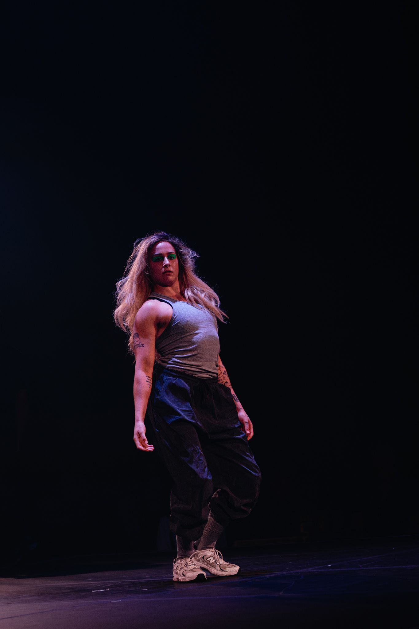 Contemporary dancer in casual attire performing expressive movements on dimly lit stage.