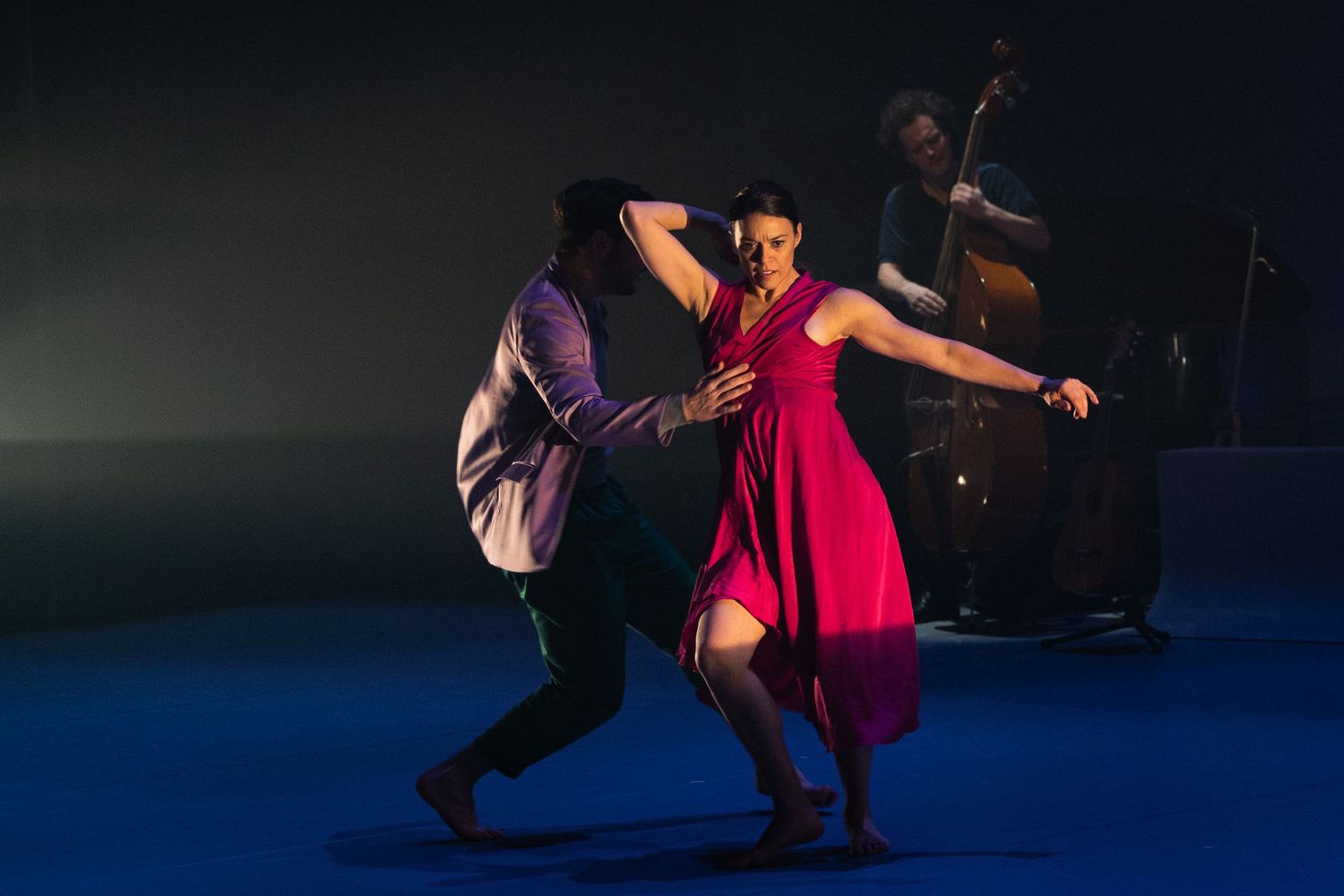 Silhouetted dancers perform powerful acrobatic moves on a dimly lit stage with blue lighting effects.