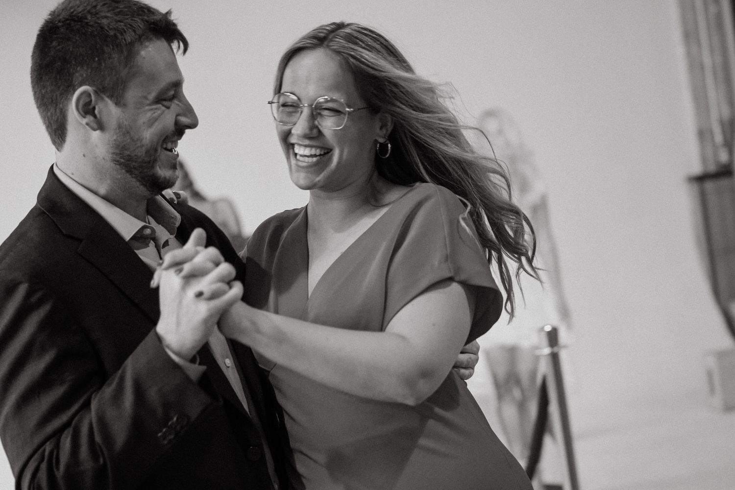 A joyful couple laughs and dances together in an intimate black and white moment captured on camera.