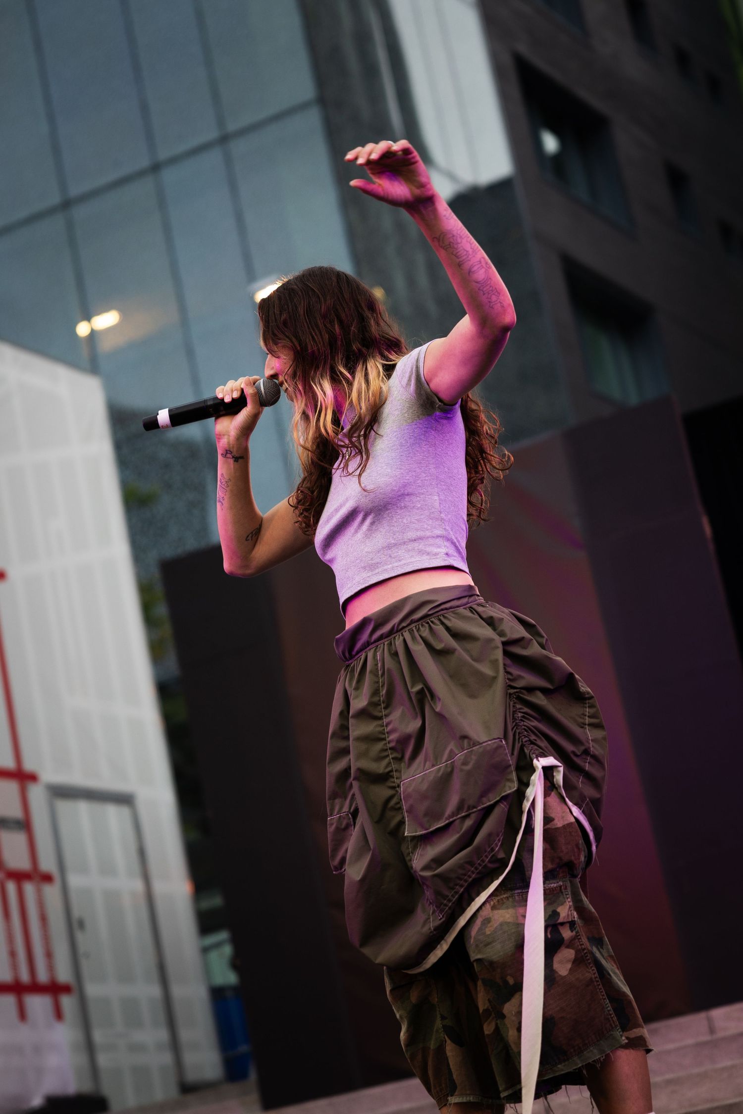 Contemporary dancer performs dynamic movements in cargo pants and pink top against modern building facade.