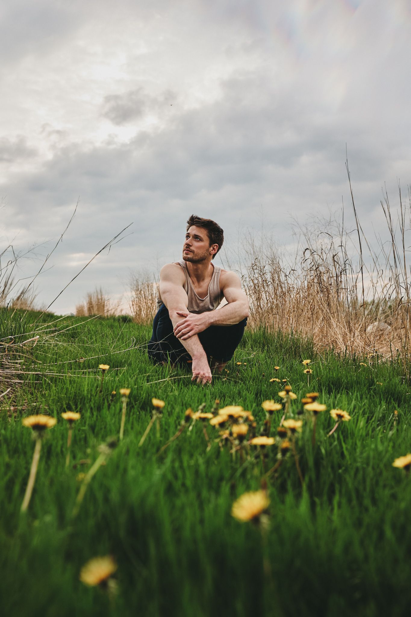 Person relaxing among yellow wildflowers in a green hillside meadow under an overcast sky.