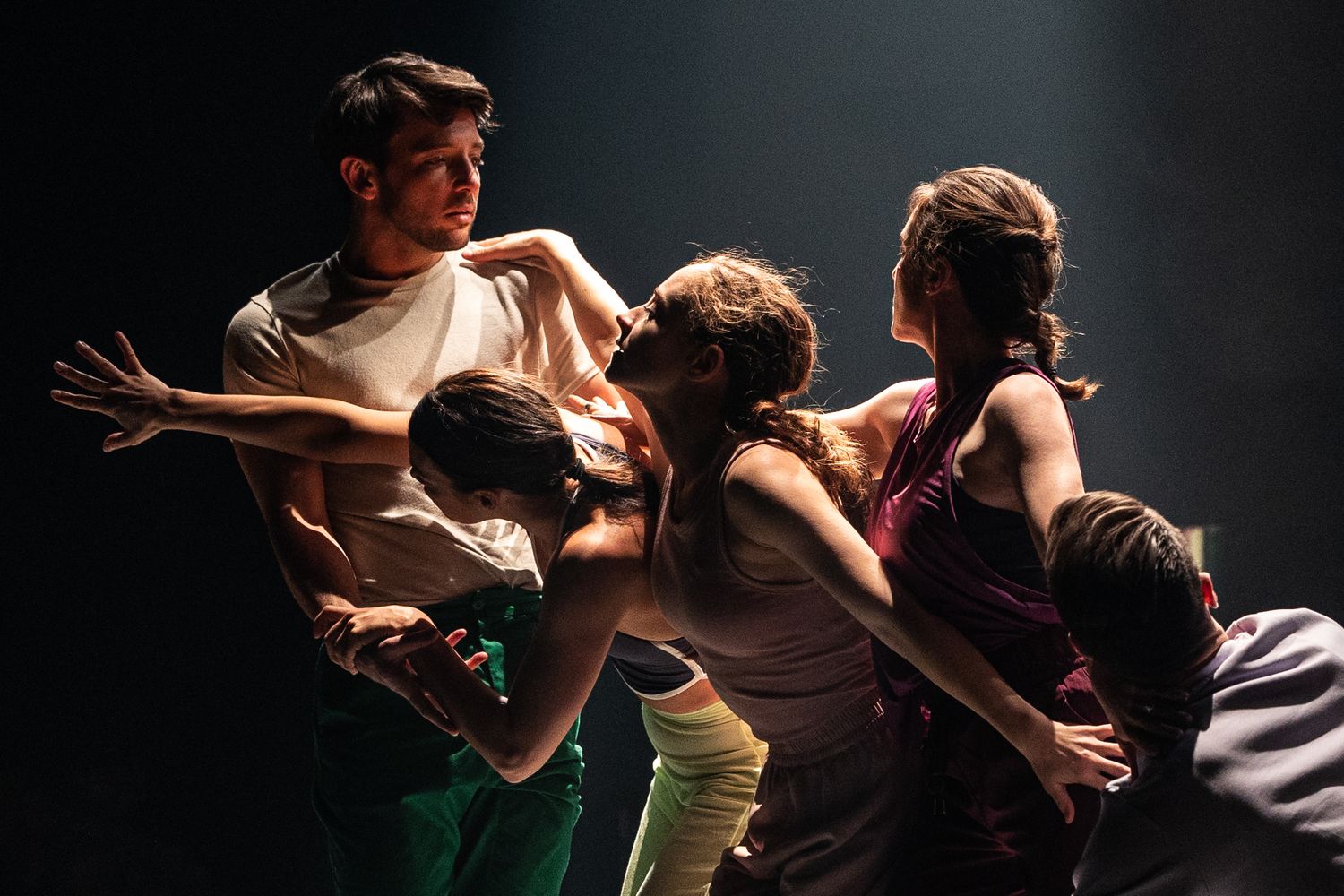 Dramatic photo sequence of contemporary dancers in mid-performance showing fluid dance movements on dark stage.