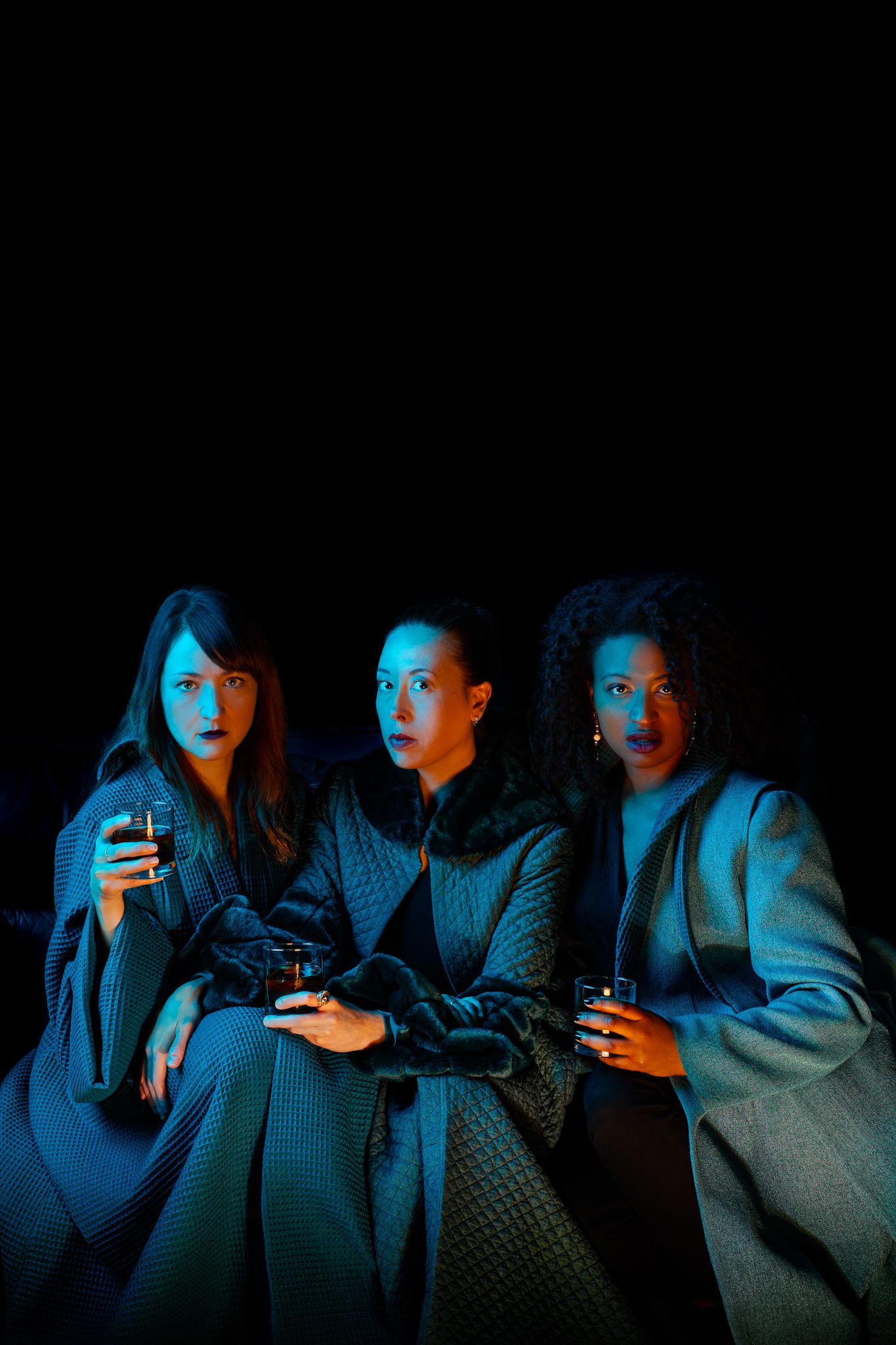 Group of people lit by blue light from mobile phone screens in dark room while looking at their devices.