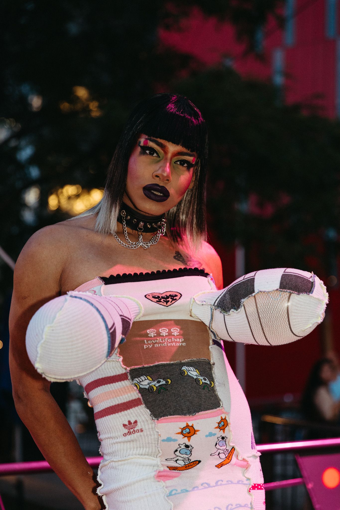 A performer in white sports-inspired outfit with pink accents holds a football while posing in dramatic pink lighting.