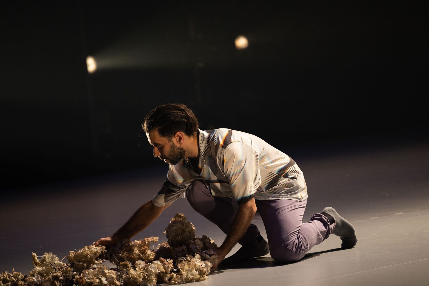 A contemporary dance performer executes an athletic movement sequence on a dimly lit stage.