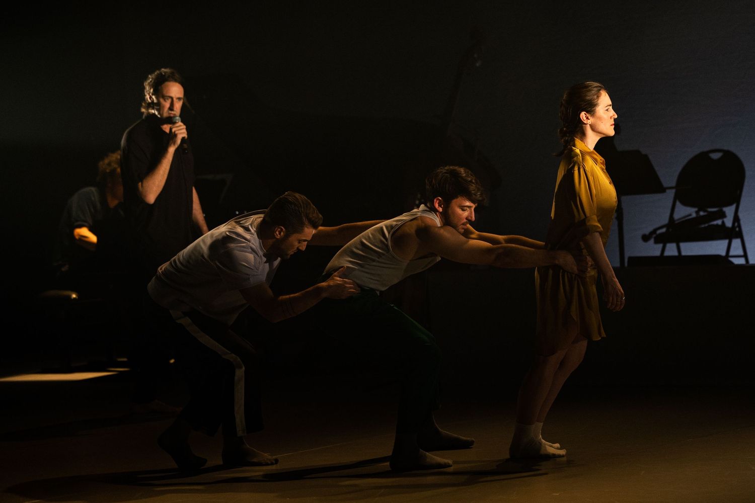 Performers on stage execute dynamic dance movements in dramatic theatrical lighting during a contemporary dance show.