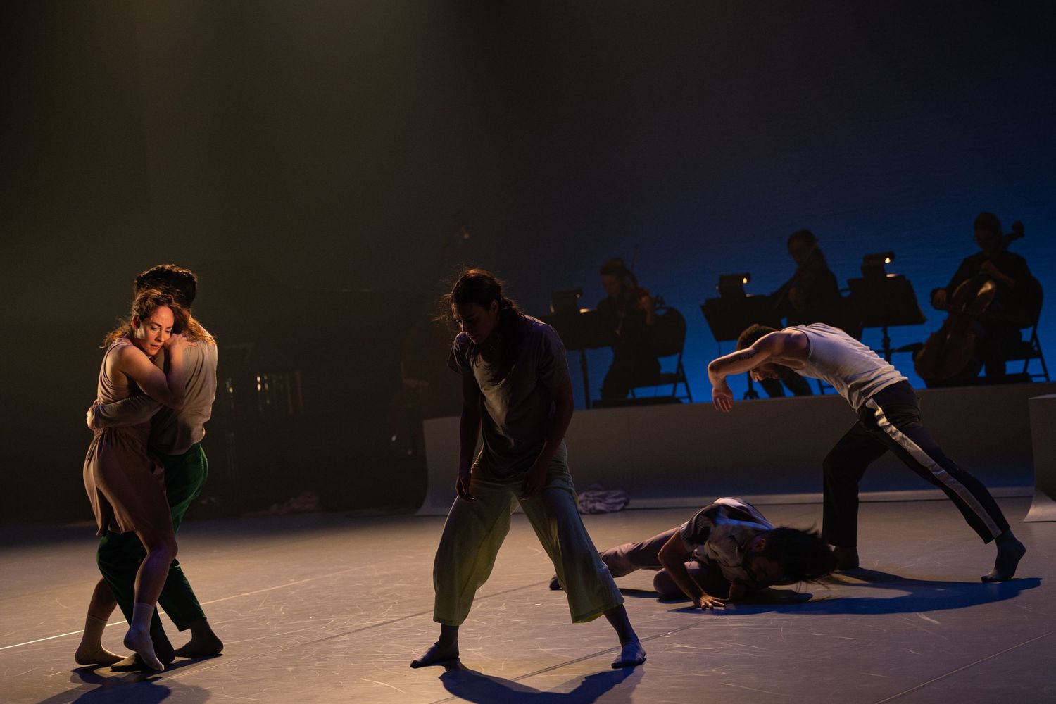 Performance artists dance in silhouette against a dark stage creating dramatic movements and shapes in low light.