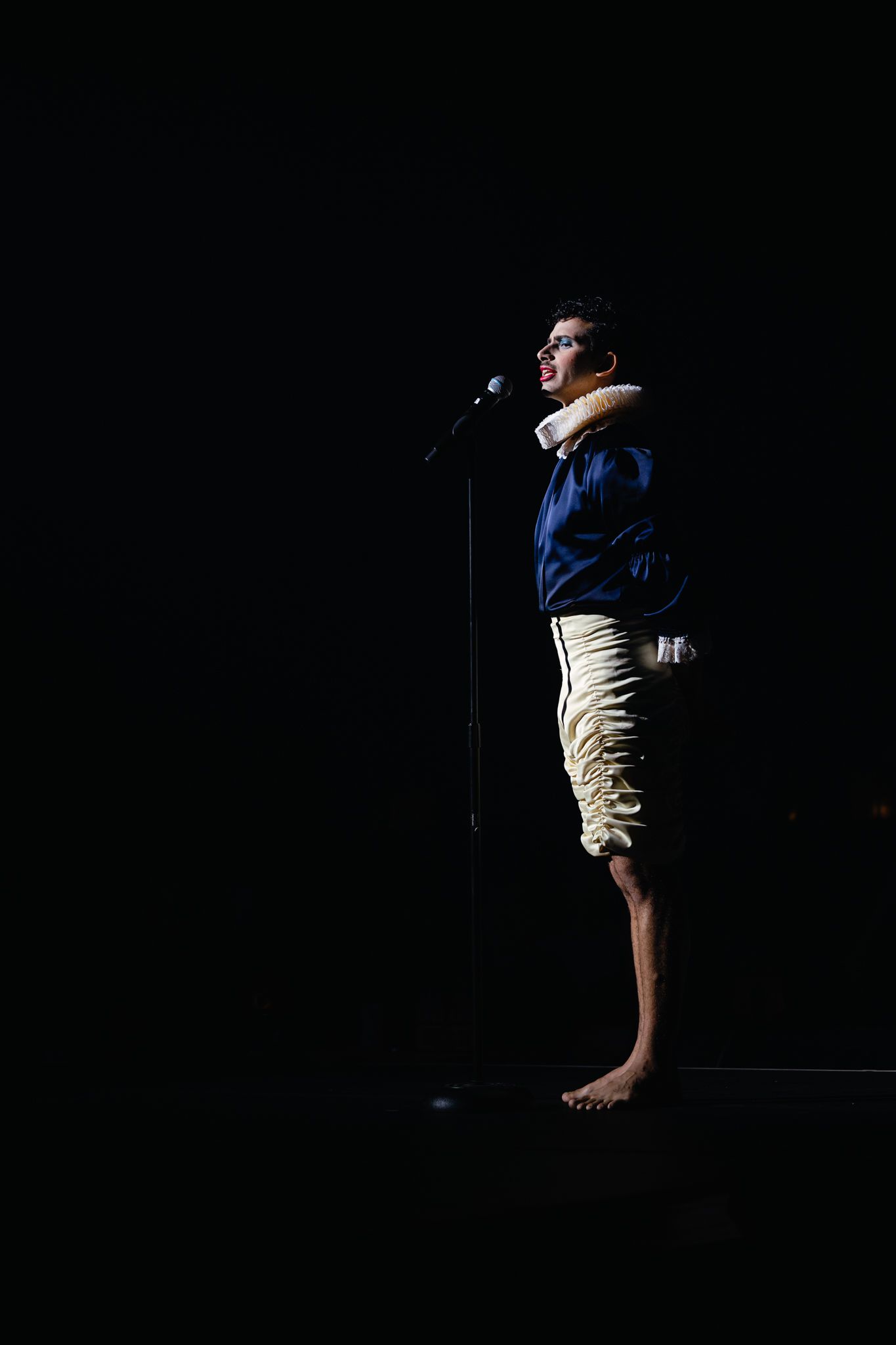 Dramatic silhouette of a performer speaking into microphone against black background.