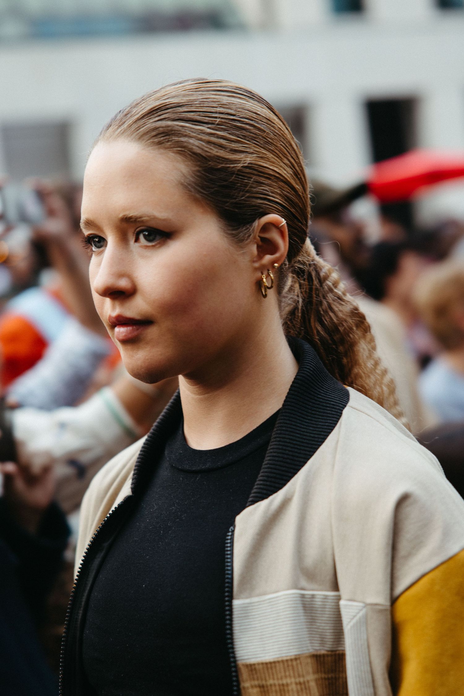 Street-style portrait of person wearing a color-block bomber jacket with brown hair pulled back in casual style.