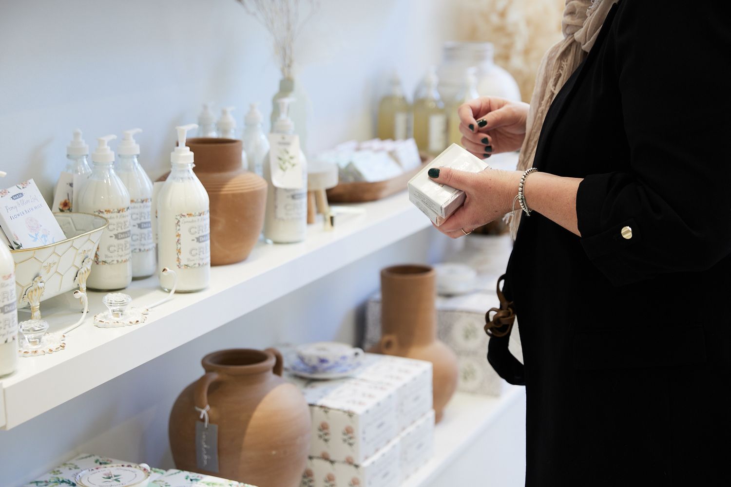 Row of glass bottles and ceramic vases arranged on a white shelf against a bright background.