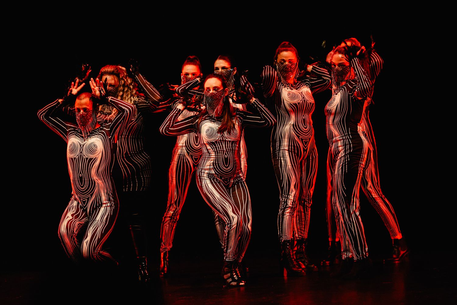 Silhouetted dancers perform in dramatic red lighting on a dark stage creating a dynamic theatrical scene.