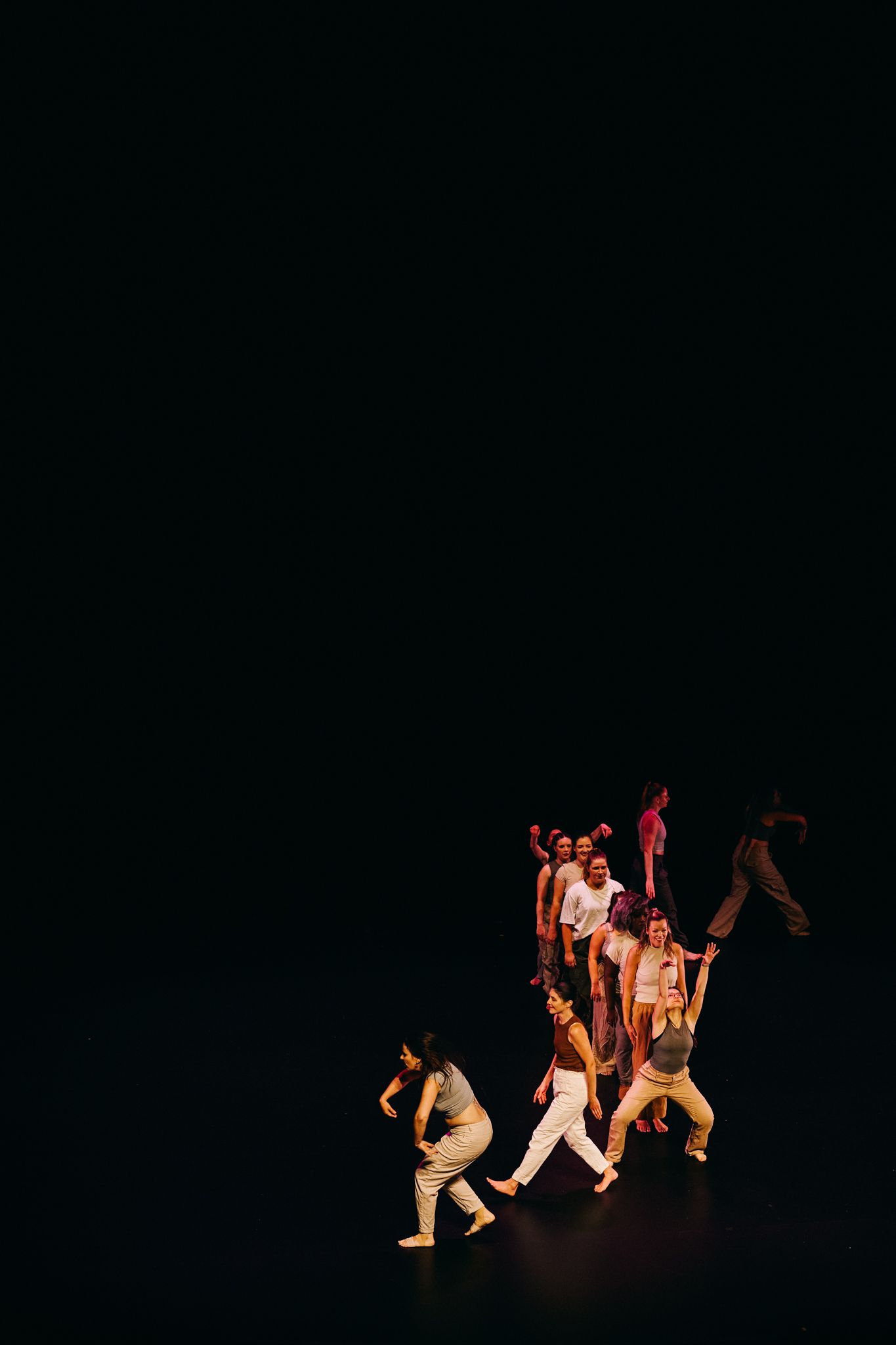 Performers in white costumes dance in dramatic formation against a dark background on stage.