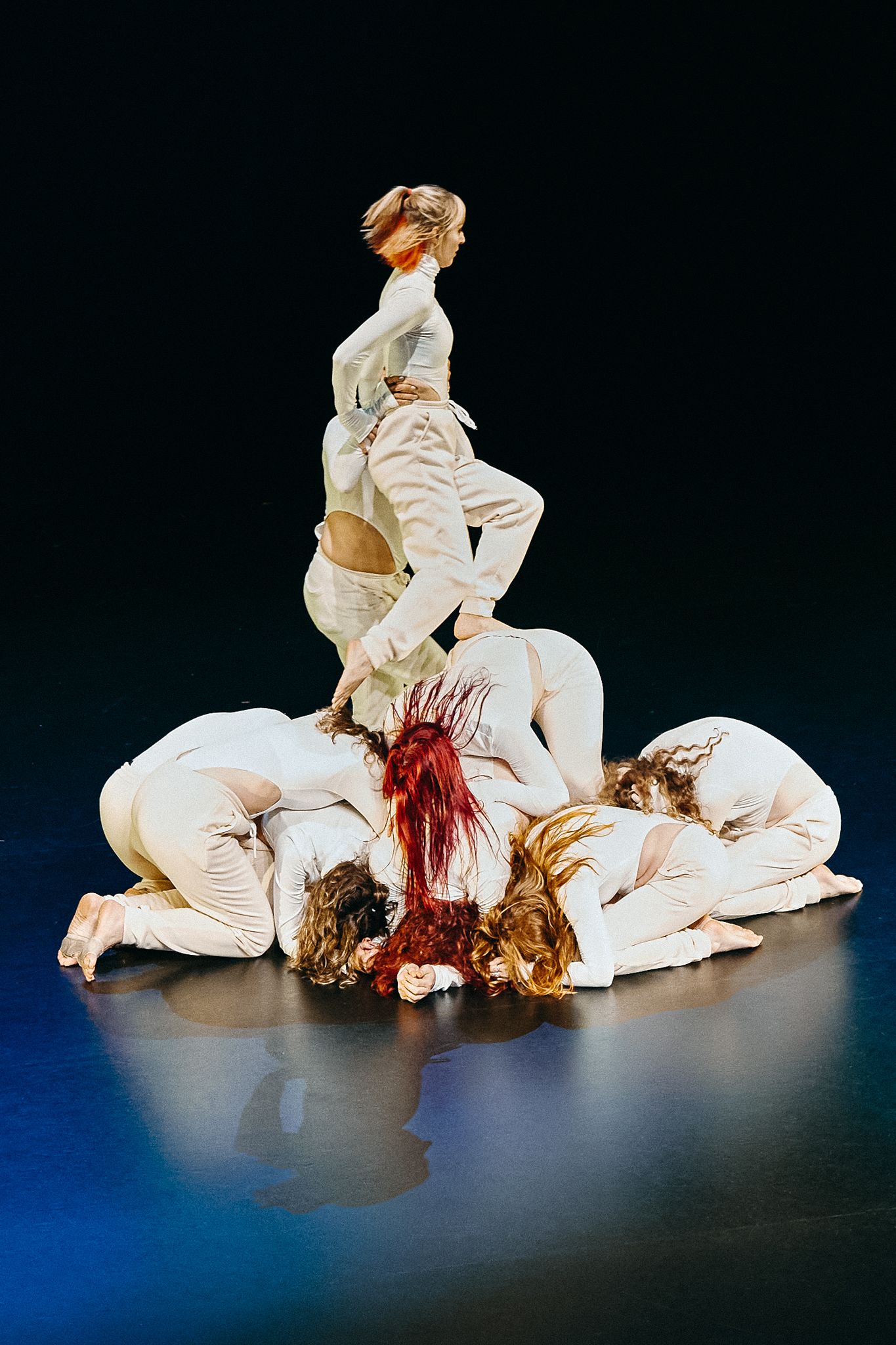 Modern dance performance featuring dancers in white costumes creating dramatic sculptural formations on stage.