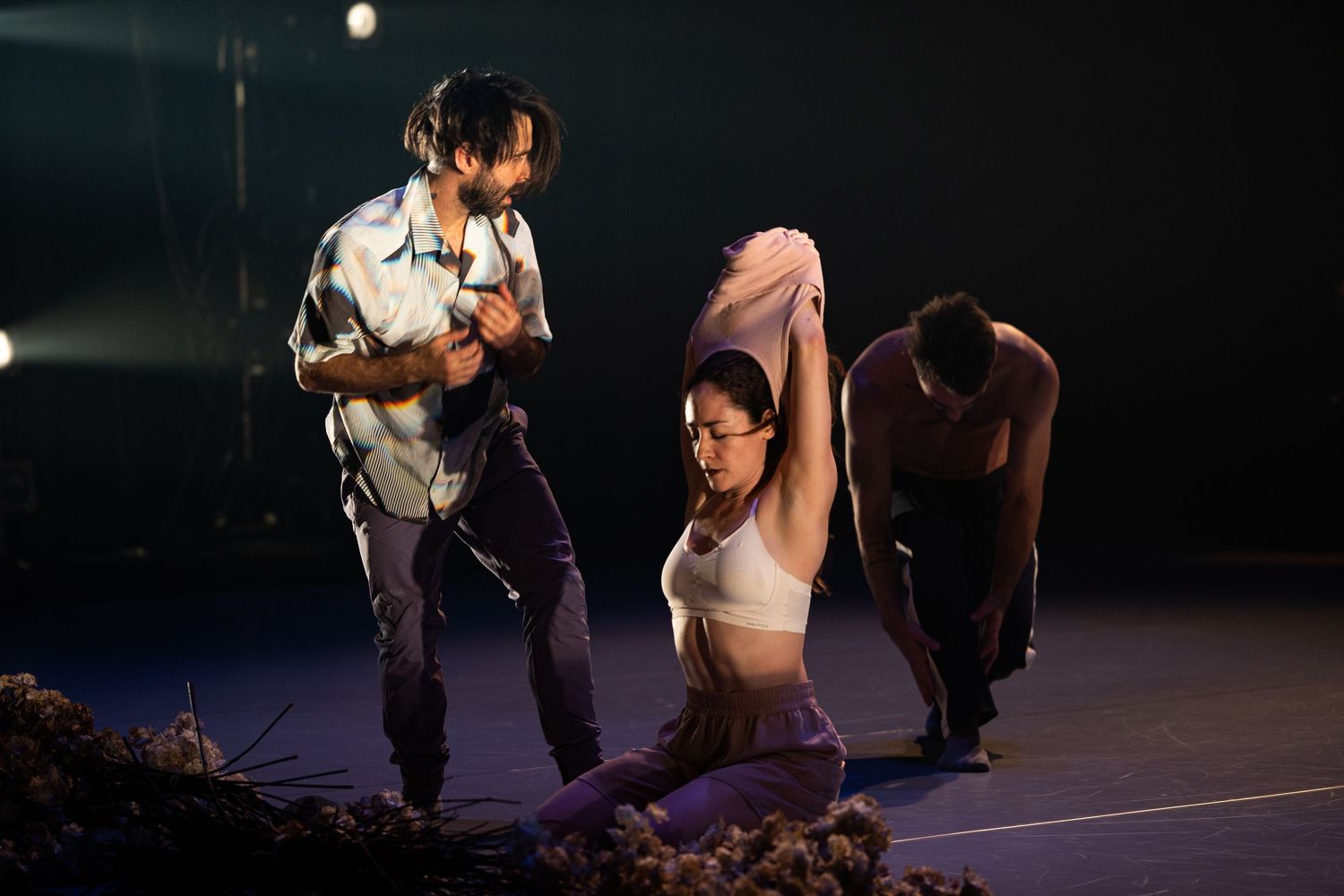 Performers in dramatic poses on a dark stage during a contemporary dance performance with dramatic lighting.