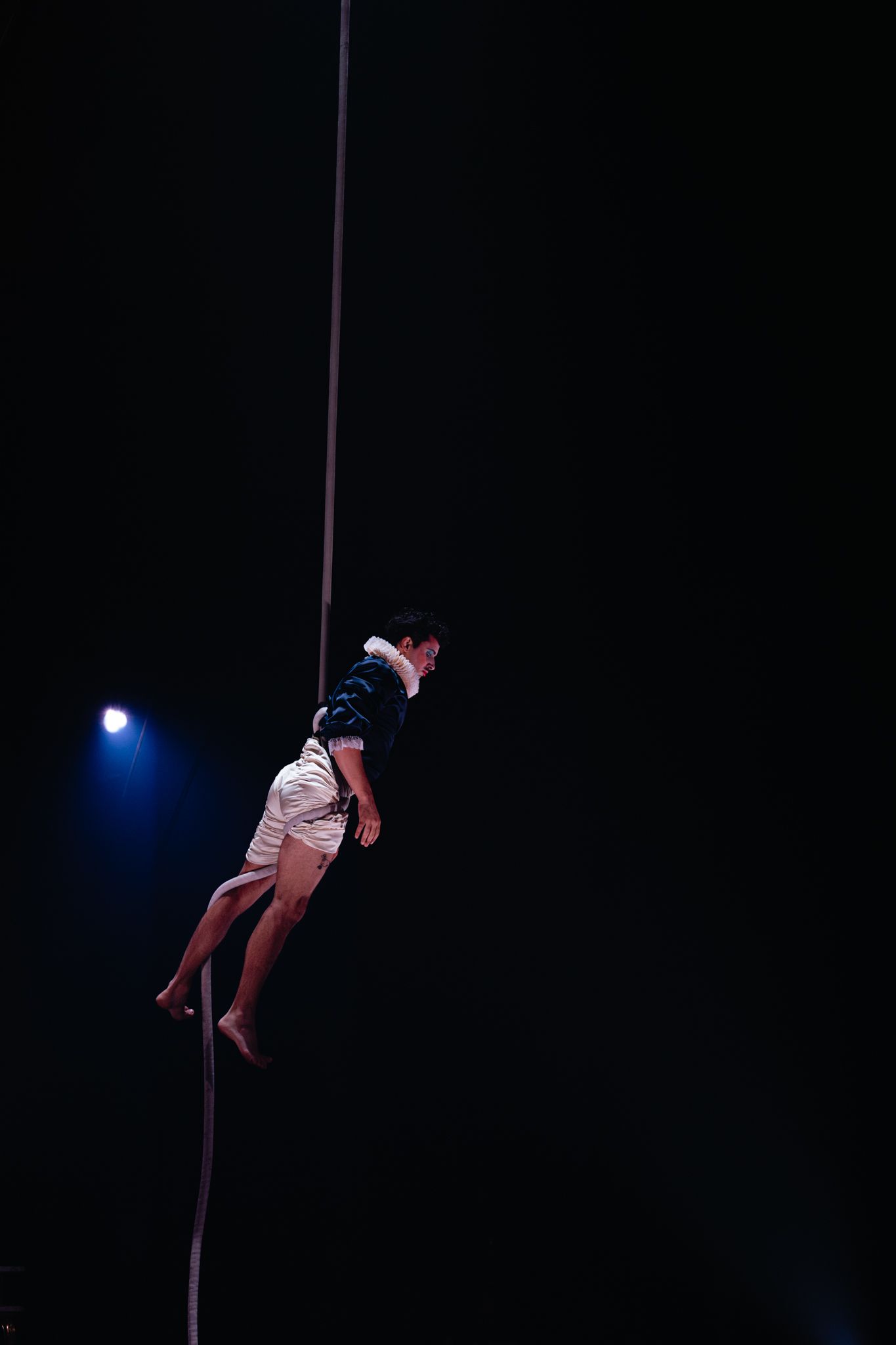 A circus performer climbs a vertical rope in dramatic lighting against a dark background during an acrobatic performance.