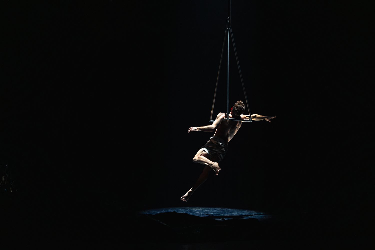 A silhouetted dancer performs a graceful leap against a dark background, creating a dramatic airborne pose.