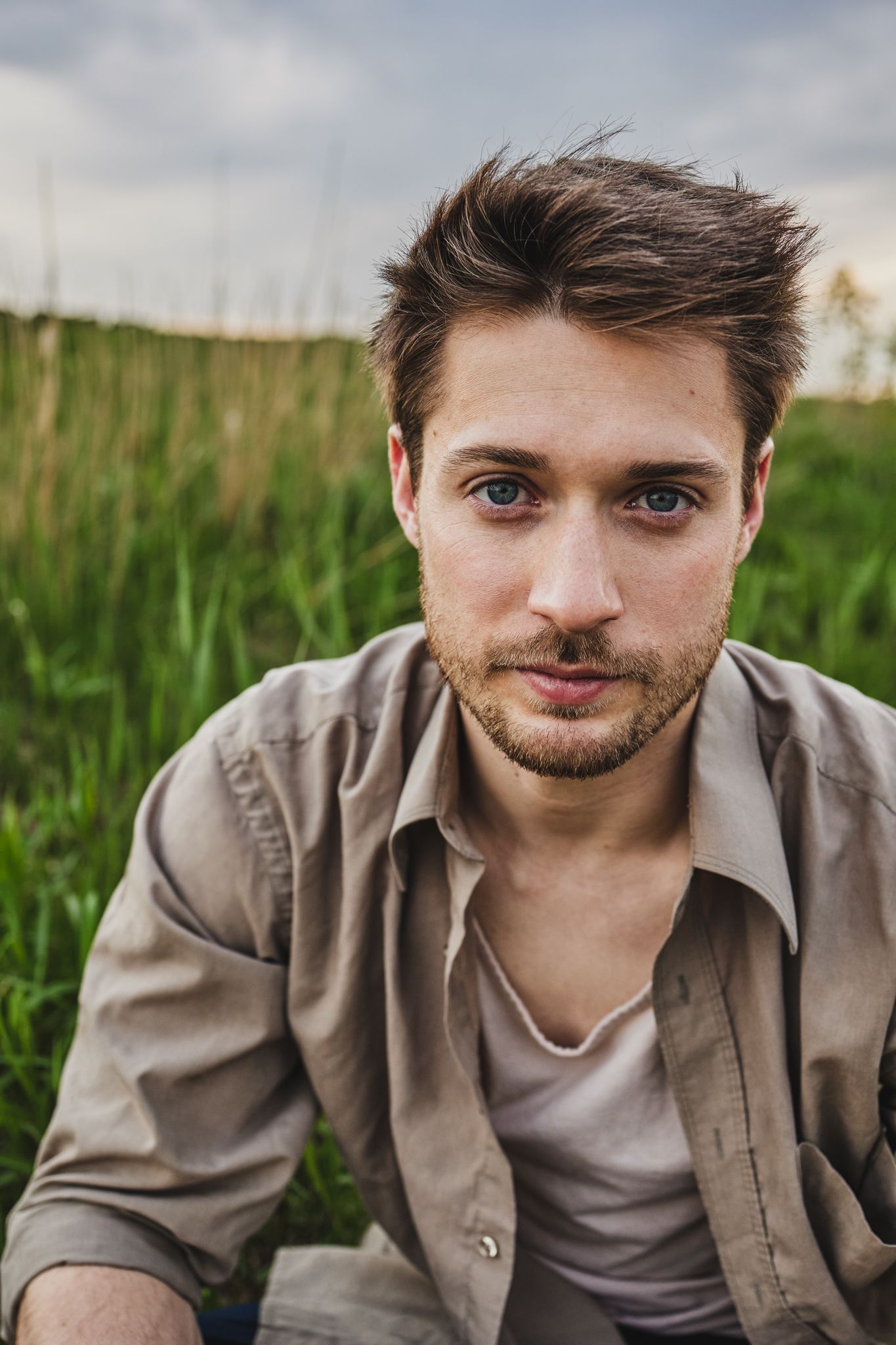 A thoughtful portrait photograph taken outdoors in a grassy field against an overcast sky.