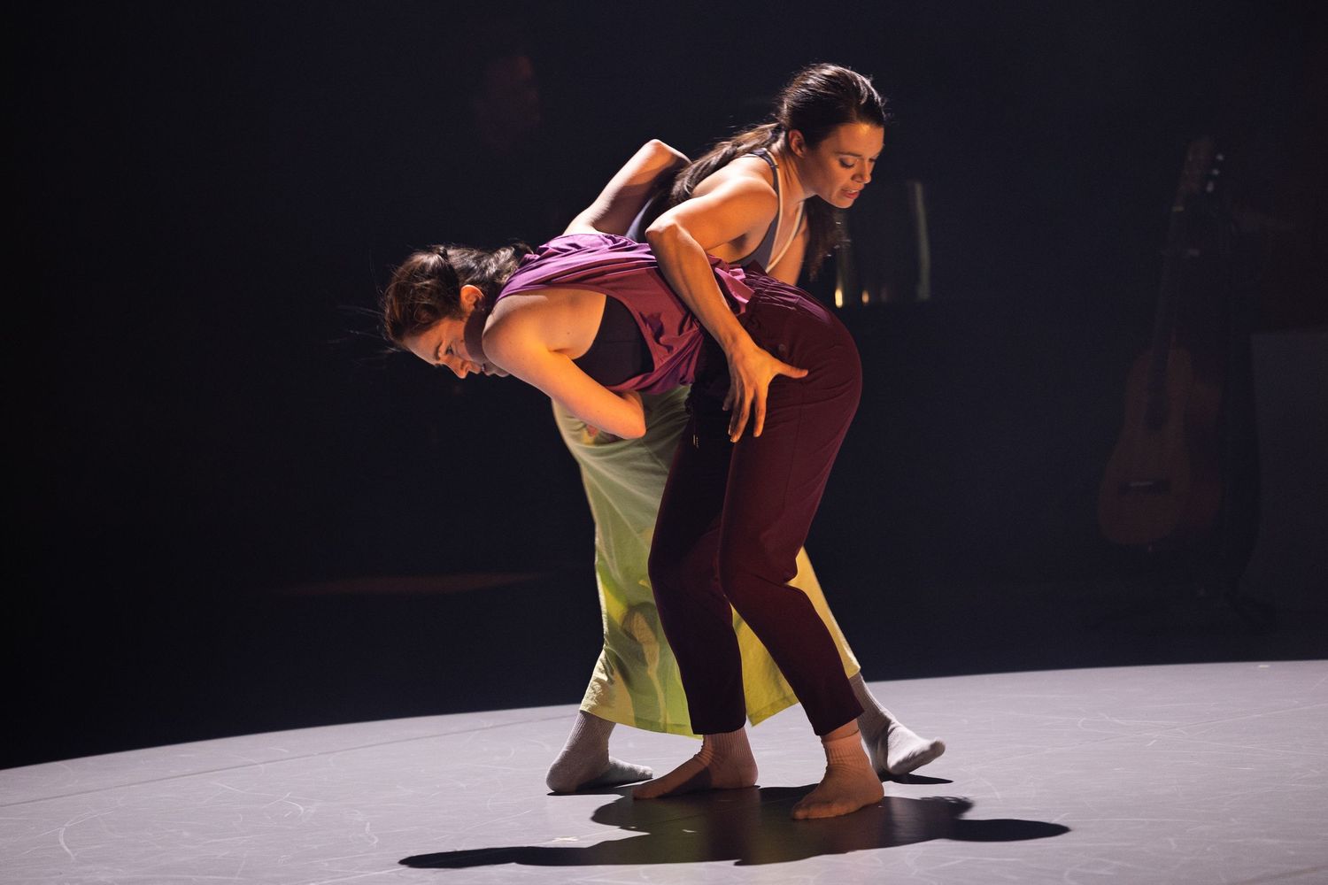 Two dancers perform a contemporary dance routine on a dimly lit stage illuminated by spotlights.