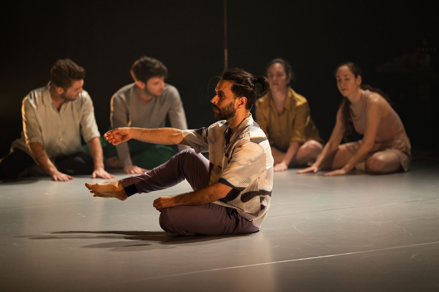 Performers sitting and lying on a dark stage floor creating abstract shapes during a contemporary dance performance.