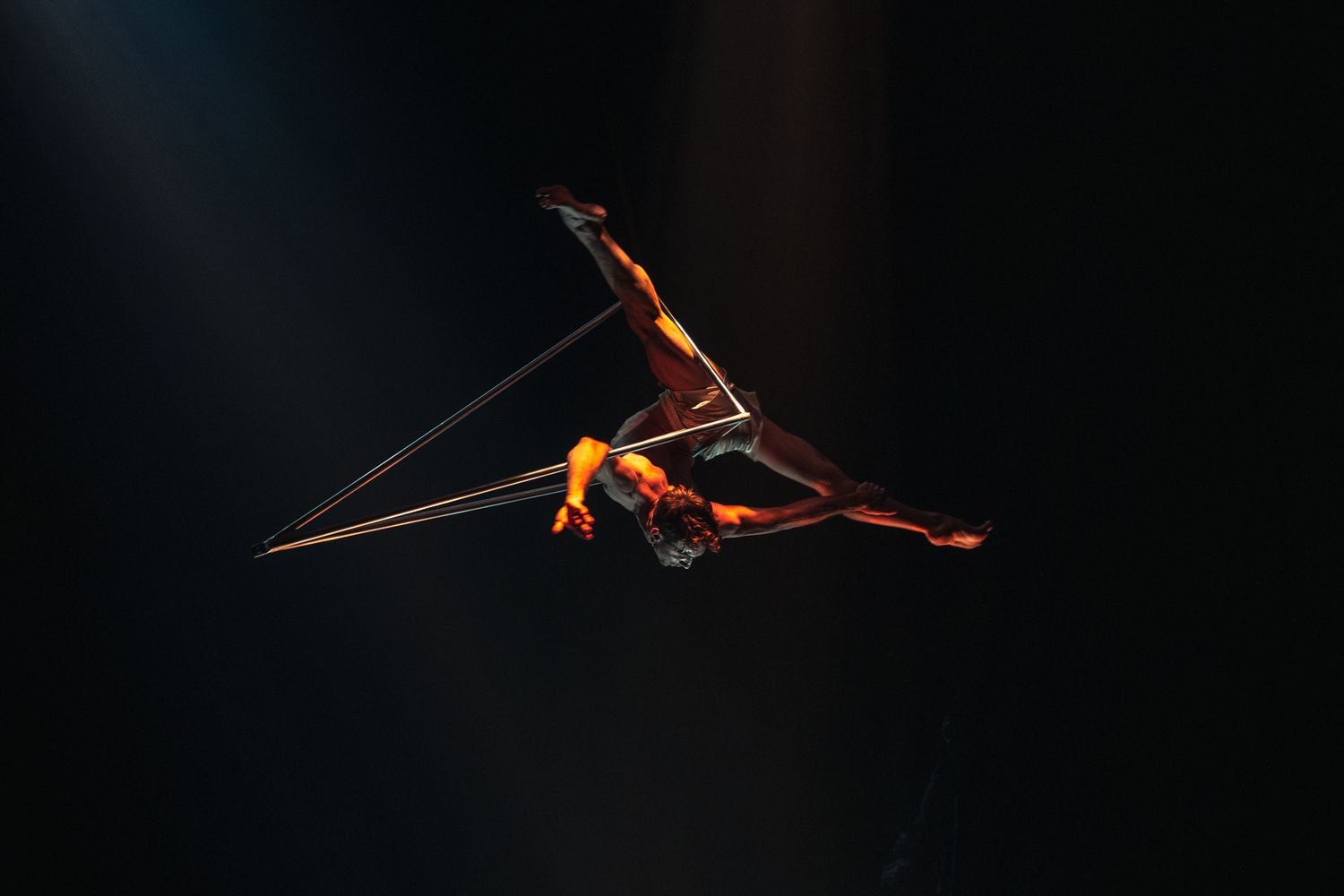 A small orange spider suspended on a delicate web thread stands out against a dark background.