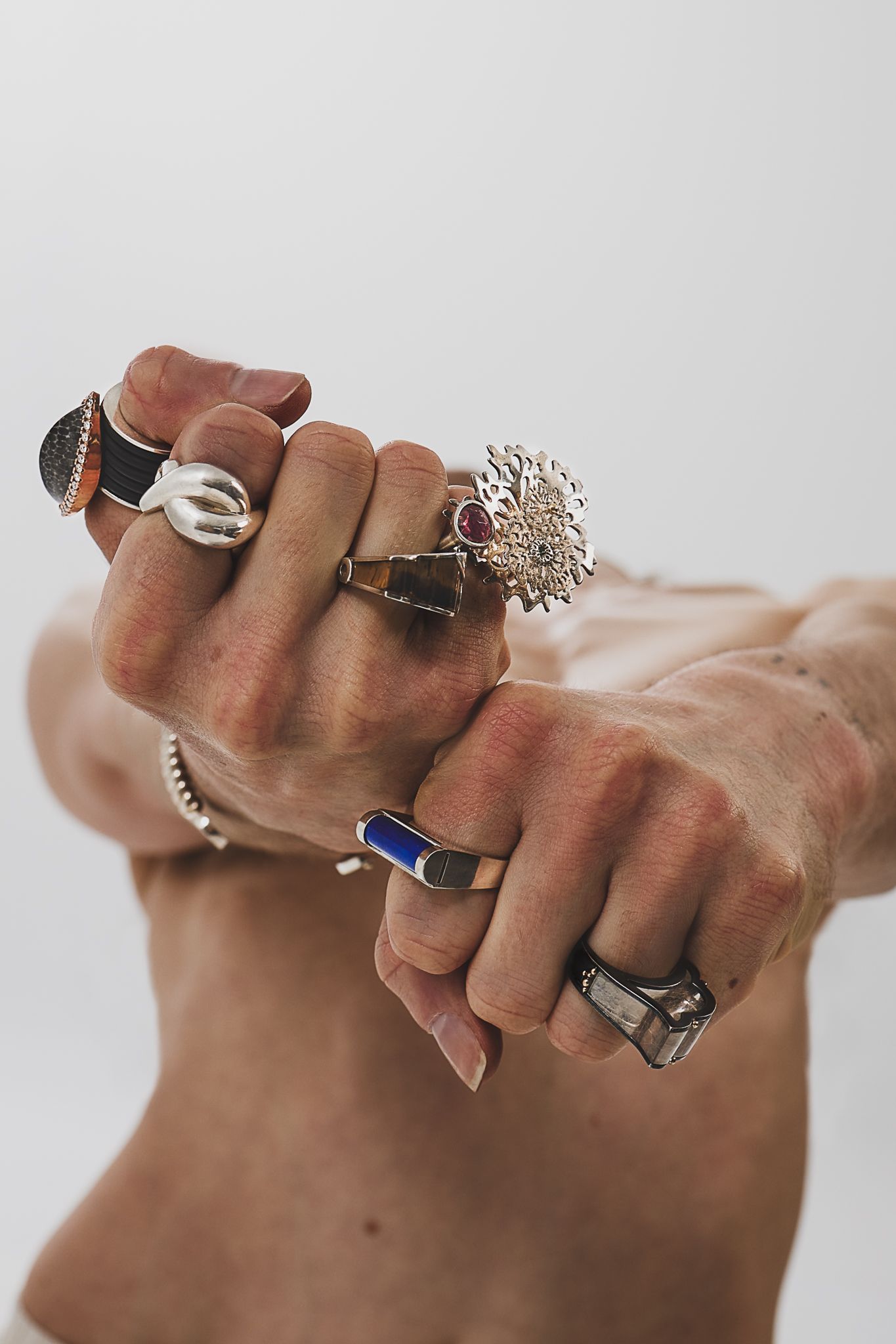 Hands wearing multiple chunky silver and gemstone rings, including a statement starburst design and colorful stone accents.