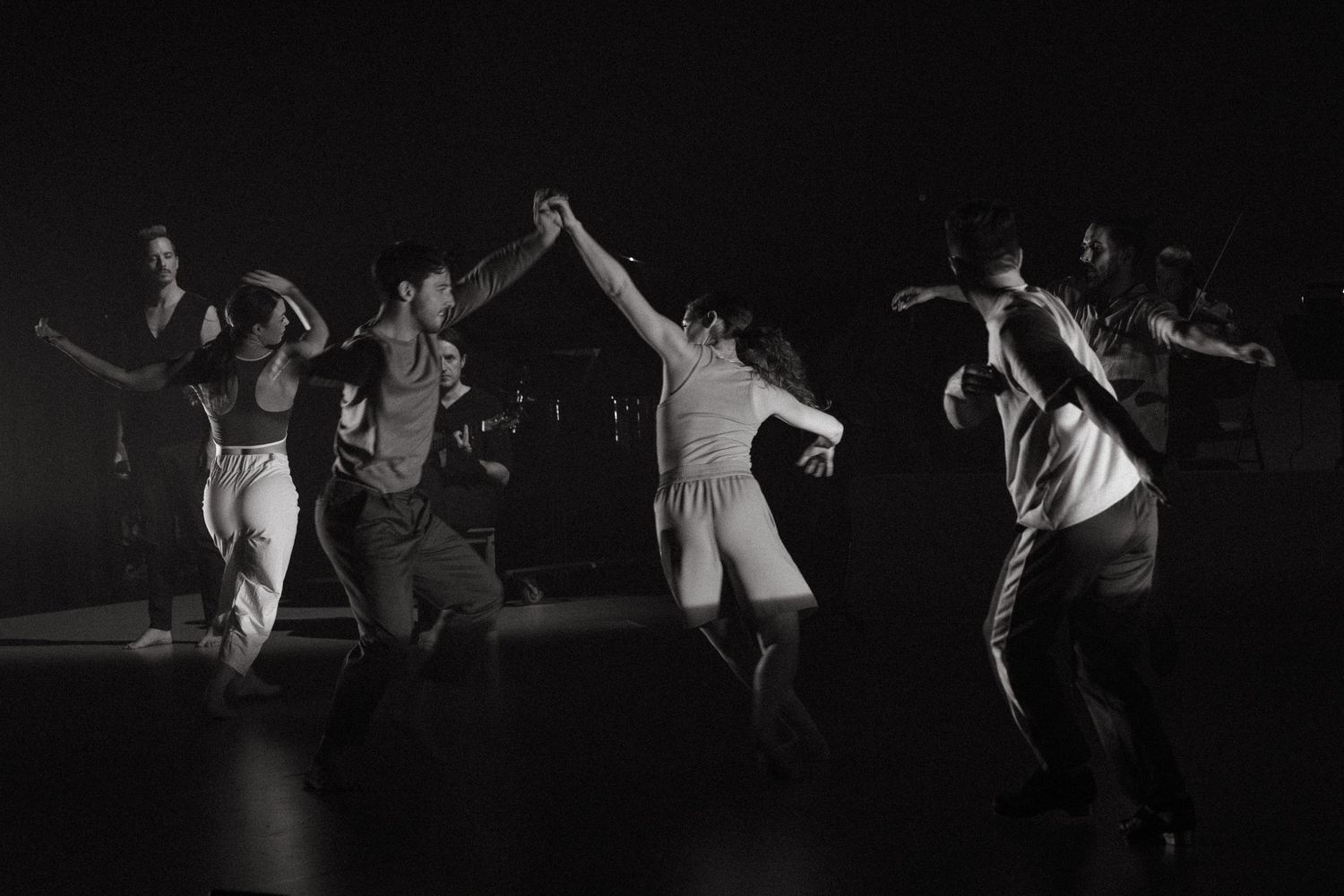 Dancers in black and white perform a dramatic sequence of leaping movements across a dark stage.