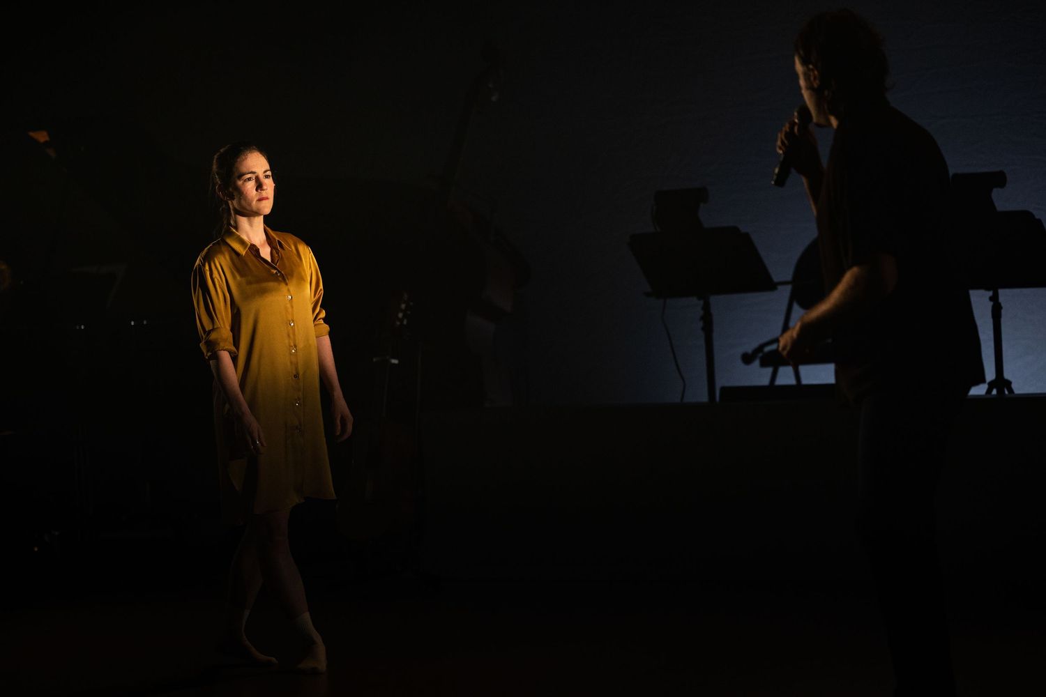 Six dark silhouettes performing on stage with dramatic lighting and shadows creating a moody atmosphere.