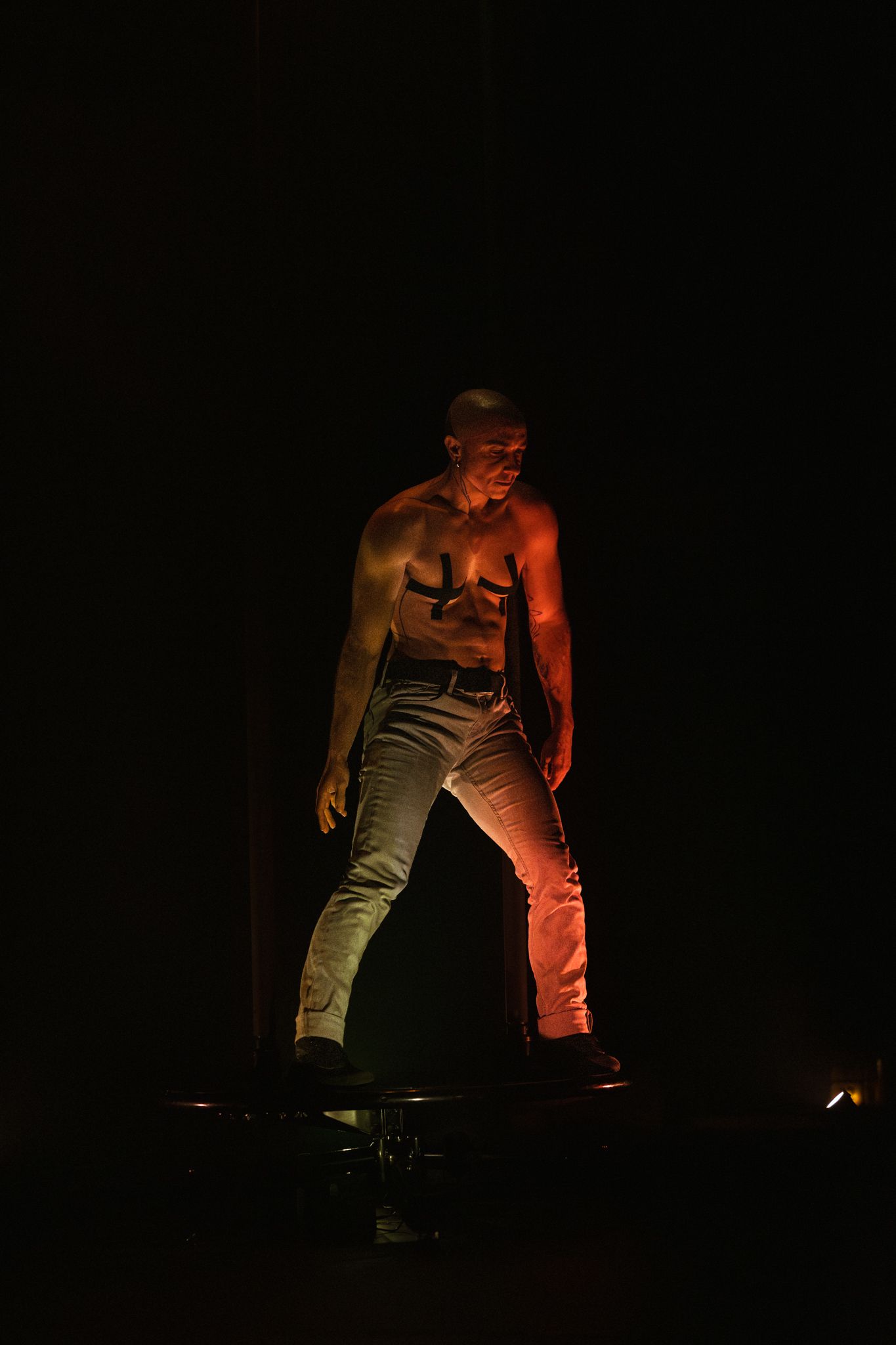 Dramatic stage performance with performer in jeans illuminated by moody red lighting on dark stage.