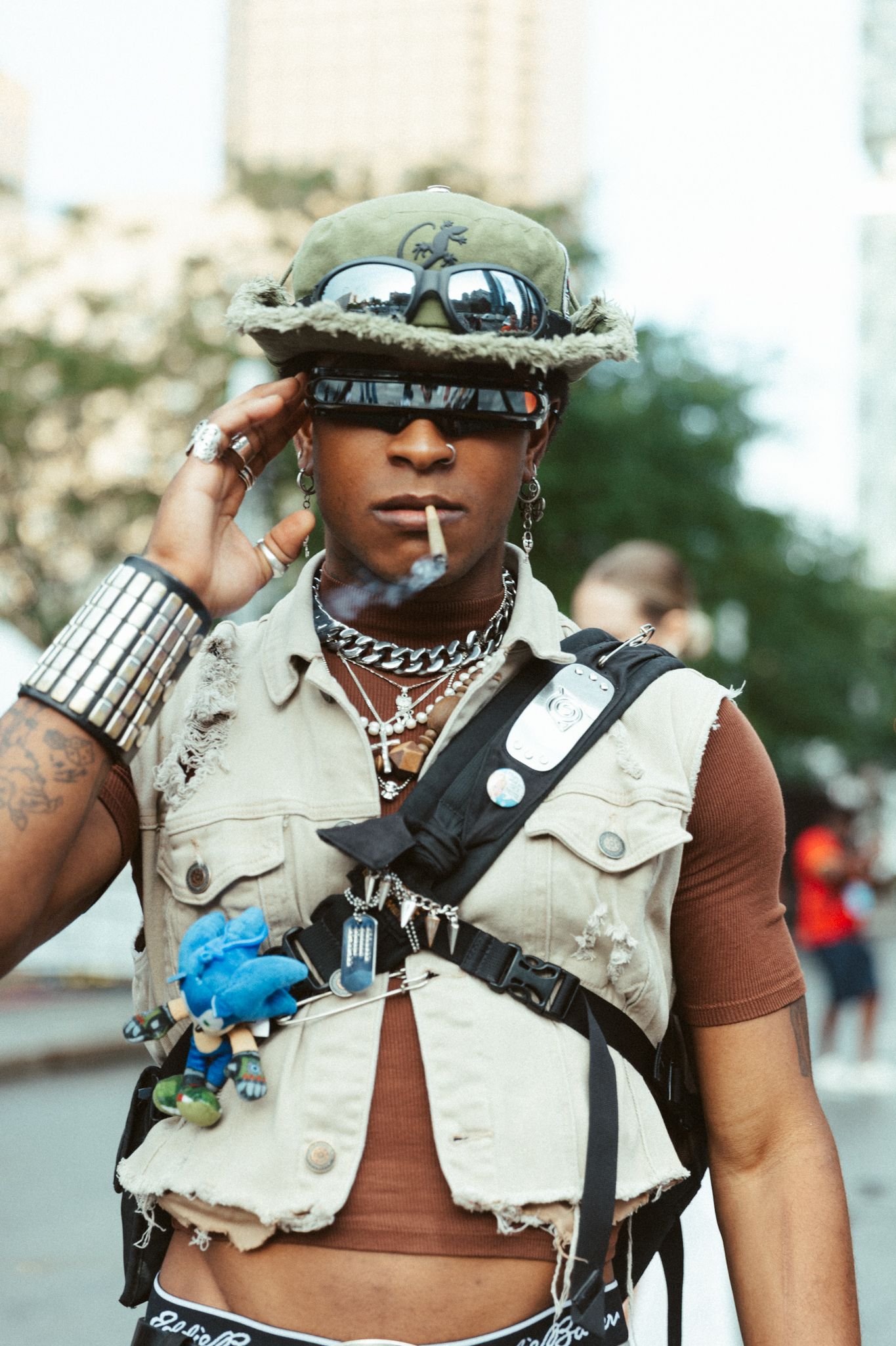 Person in sunglasses and military-style vest poses with decorative accessories at an outdoor event.