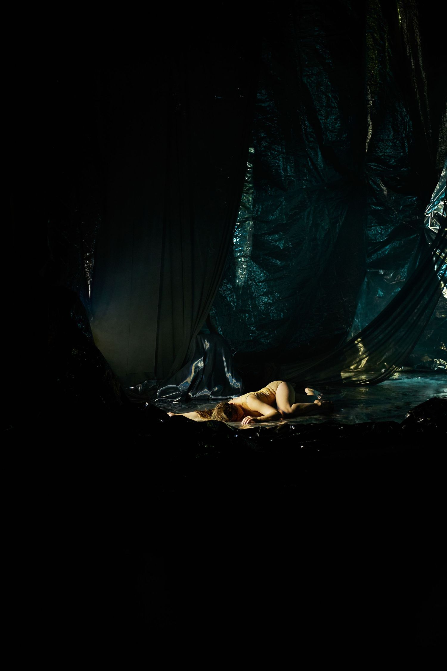 A dramatic dark wooded scene illuminated by moody lighting with a figure lying on the mossy forest floor.