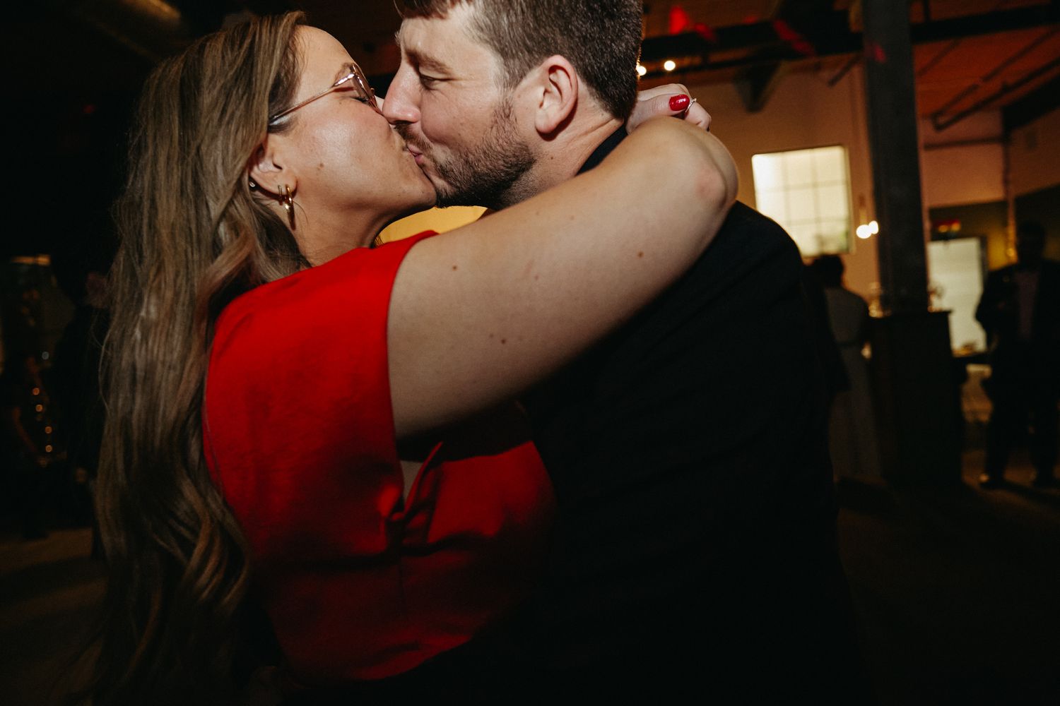 A couple sharing an intimate embrace and kiss in a dimly lit indoor setting.