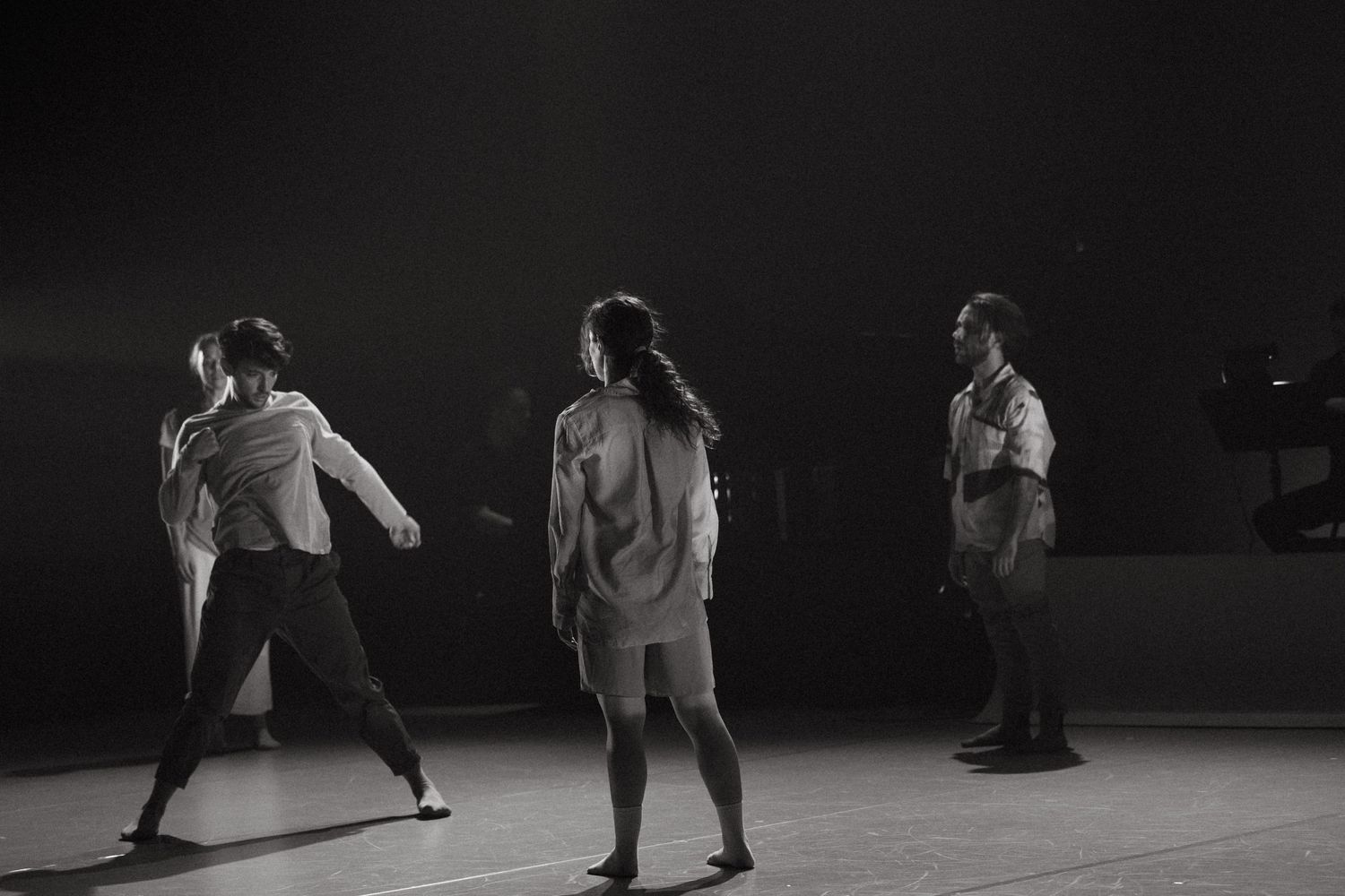 Three dancers perform in silhouette on a dark stage captured in black and white photography during a performance.
