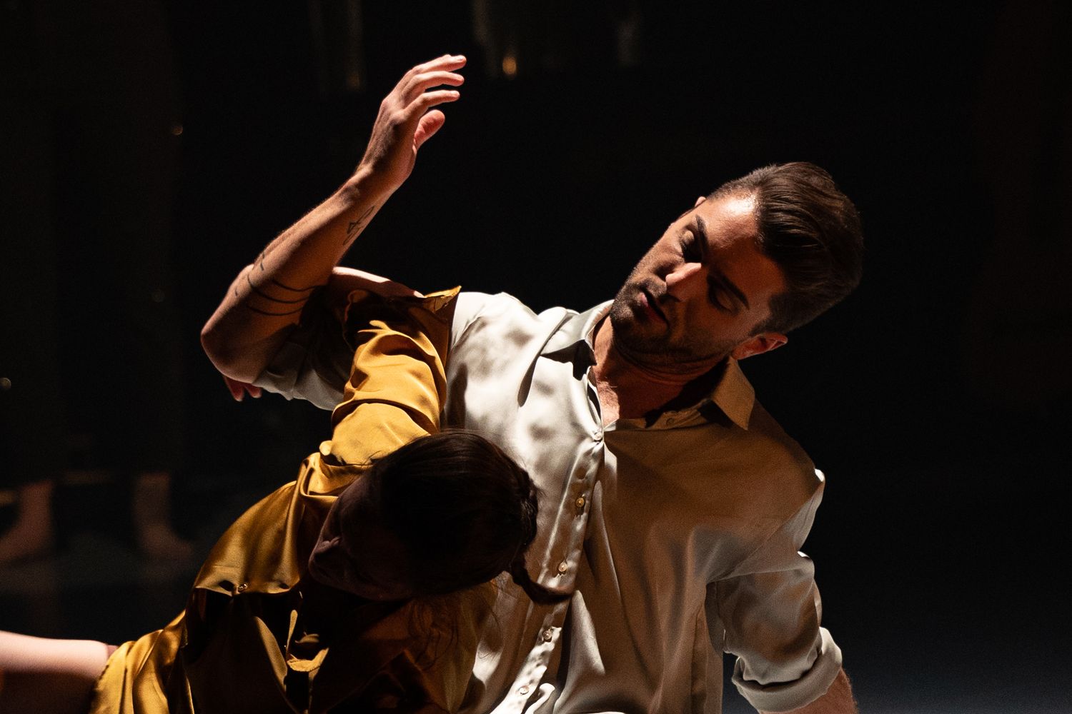 Dancers in yellow and white costumes perform an expressive contemporary dance piece on a dark stage.