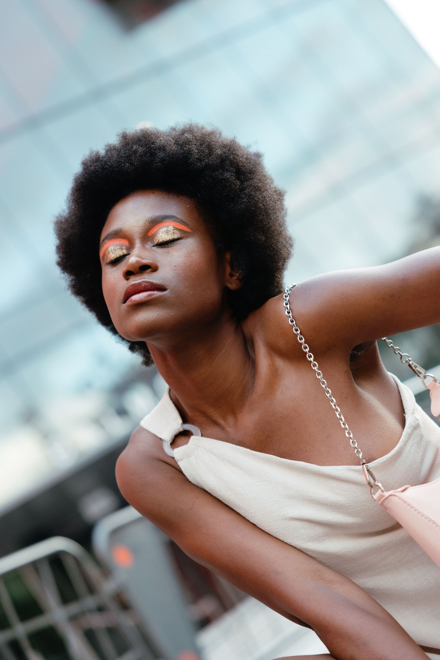 Person wearing cream-colored top with natural afro hairstyle tilts head back with eyes closed in dreamy pose outdoors.