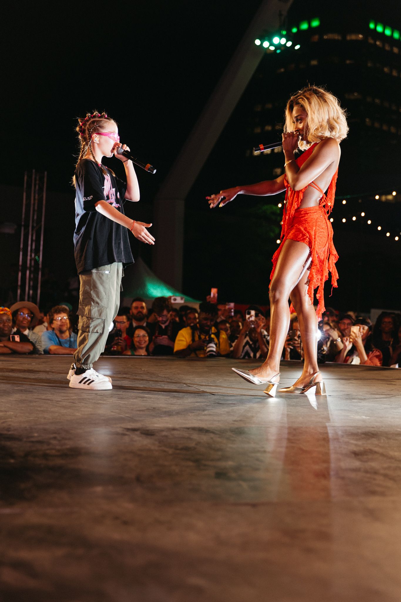 Two performers in contrasting outfits engage in a dynamic dance performance on stage with green lights in the background.