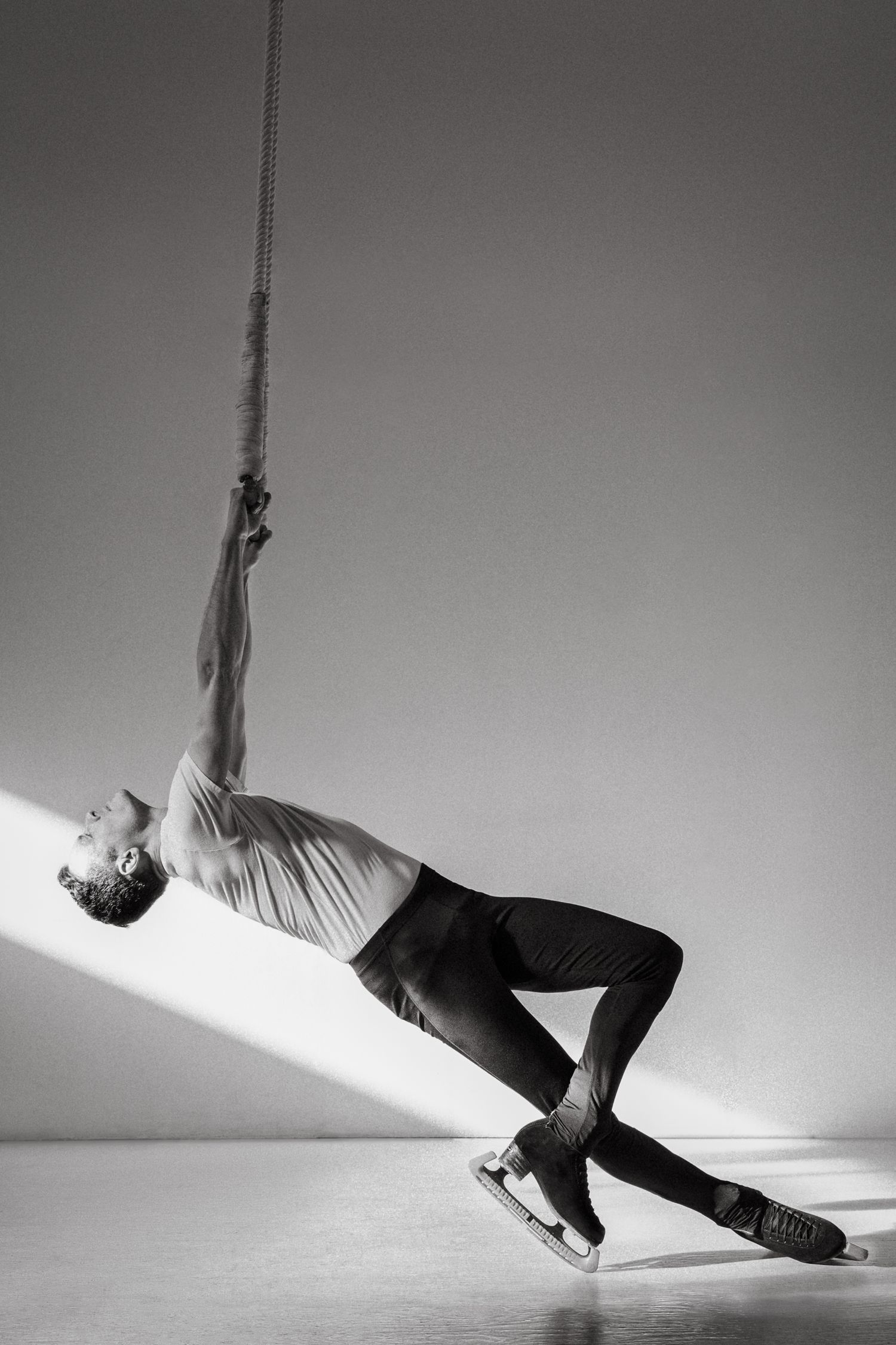 A dramatic black and white photo of a performer in athletic wear arching backwards while suspended from a rope.