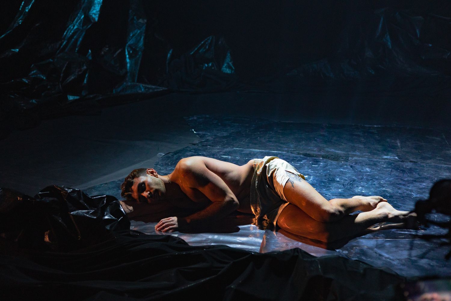 A person lying on the dark ground near water in dramatic lighting.