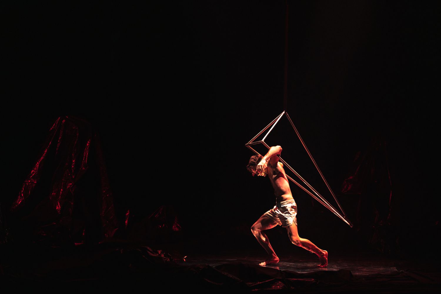 A performer in the spotlight holds an illuminated triangular prop during a dramatic stage performance.