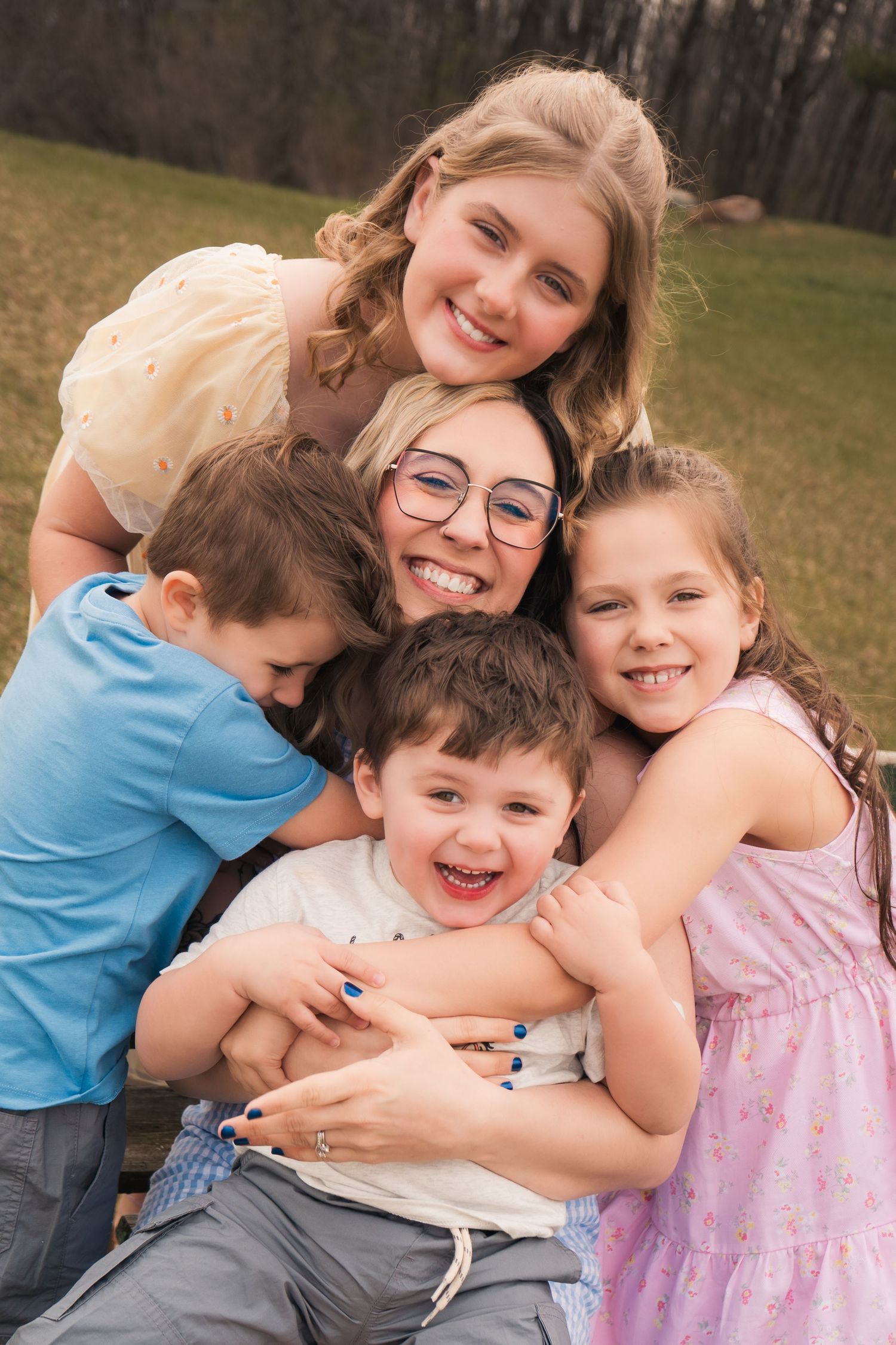 Joyful family group hug outdoors with children in casual spring attire.