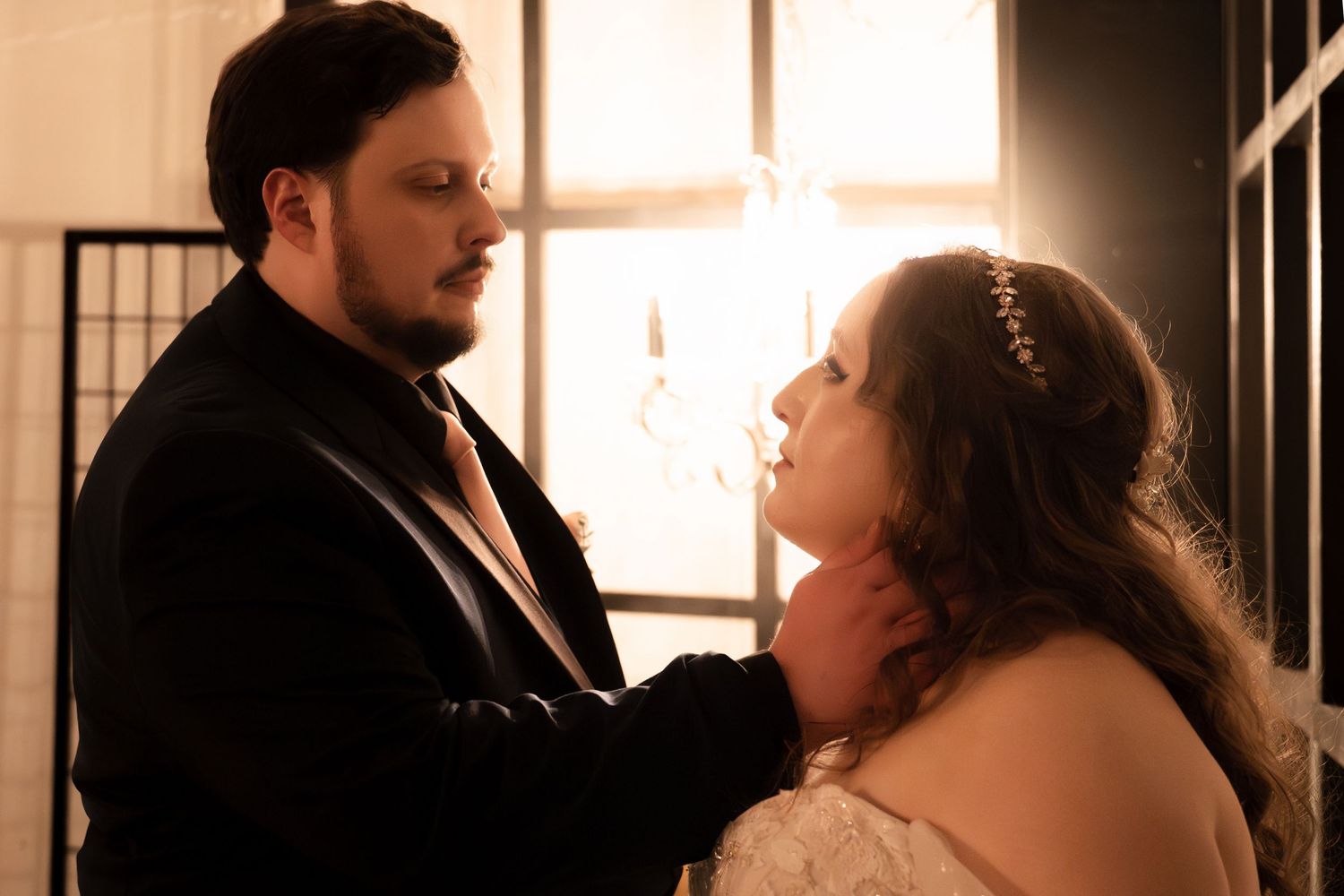 A bride and groom share an intimate moment, with soft backlit glow highlighting their wedding attire.