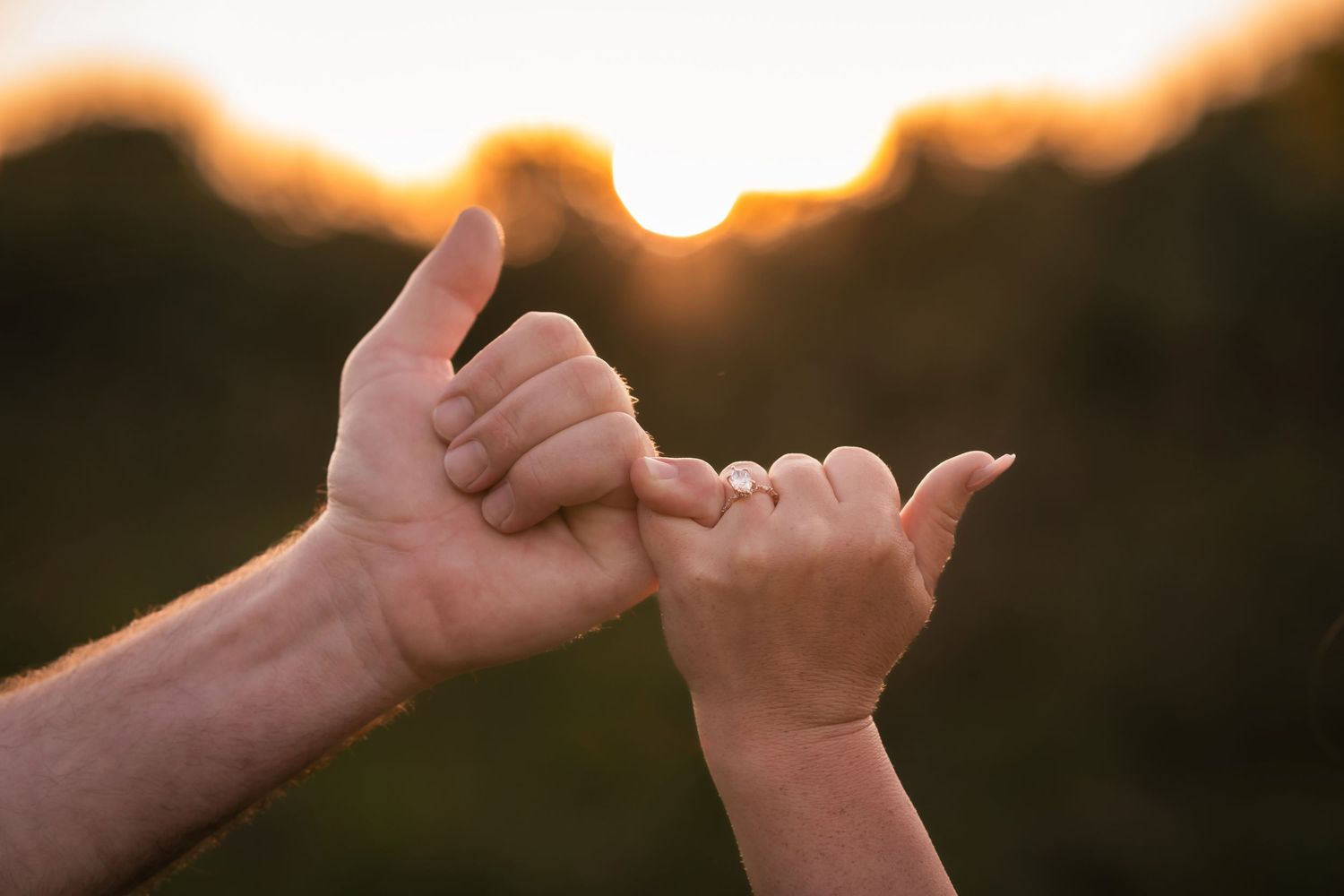 Two hands making pinky promise gesture at golden sunset, symbolizing trust and commitment outdoors.