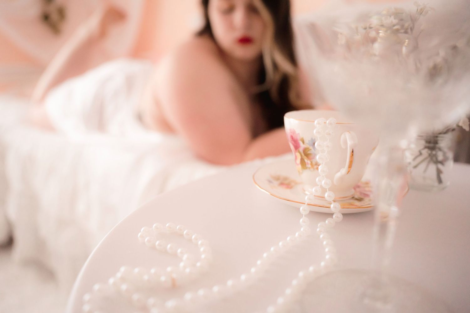 A soft focus pink-toned photo featuring an elegant teacup and saucer with dreamy lighting.