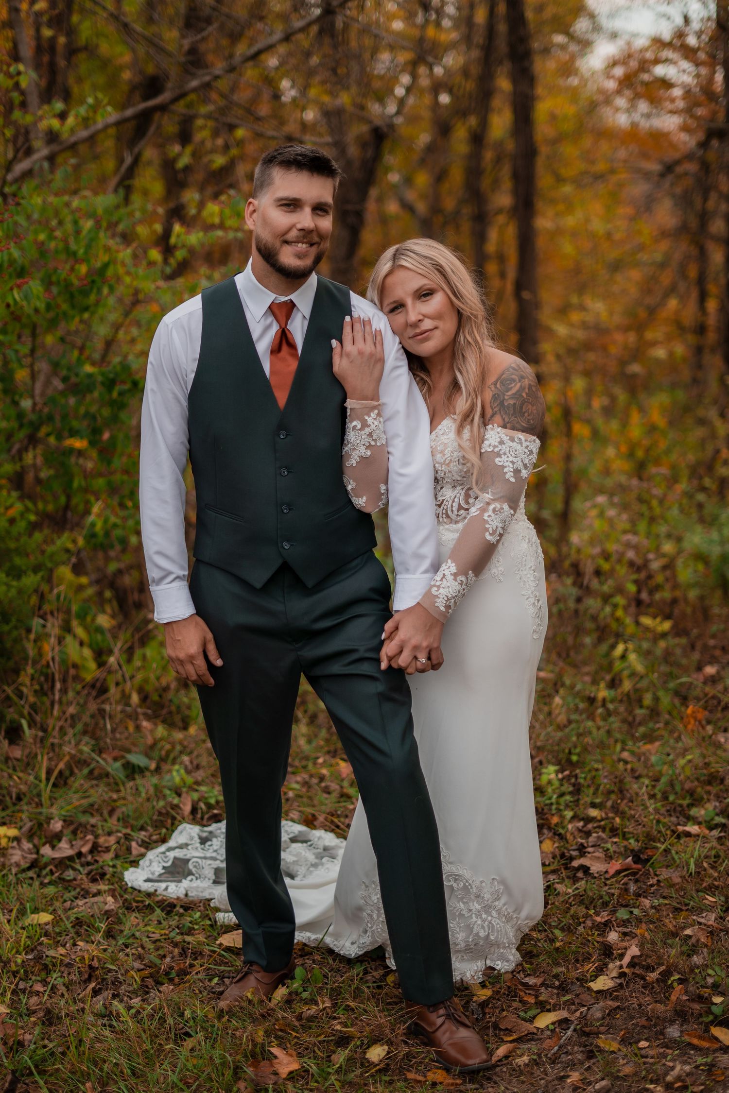 Wedding couple in formal attire posing among autumn foliage.